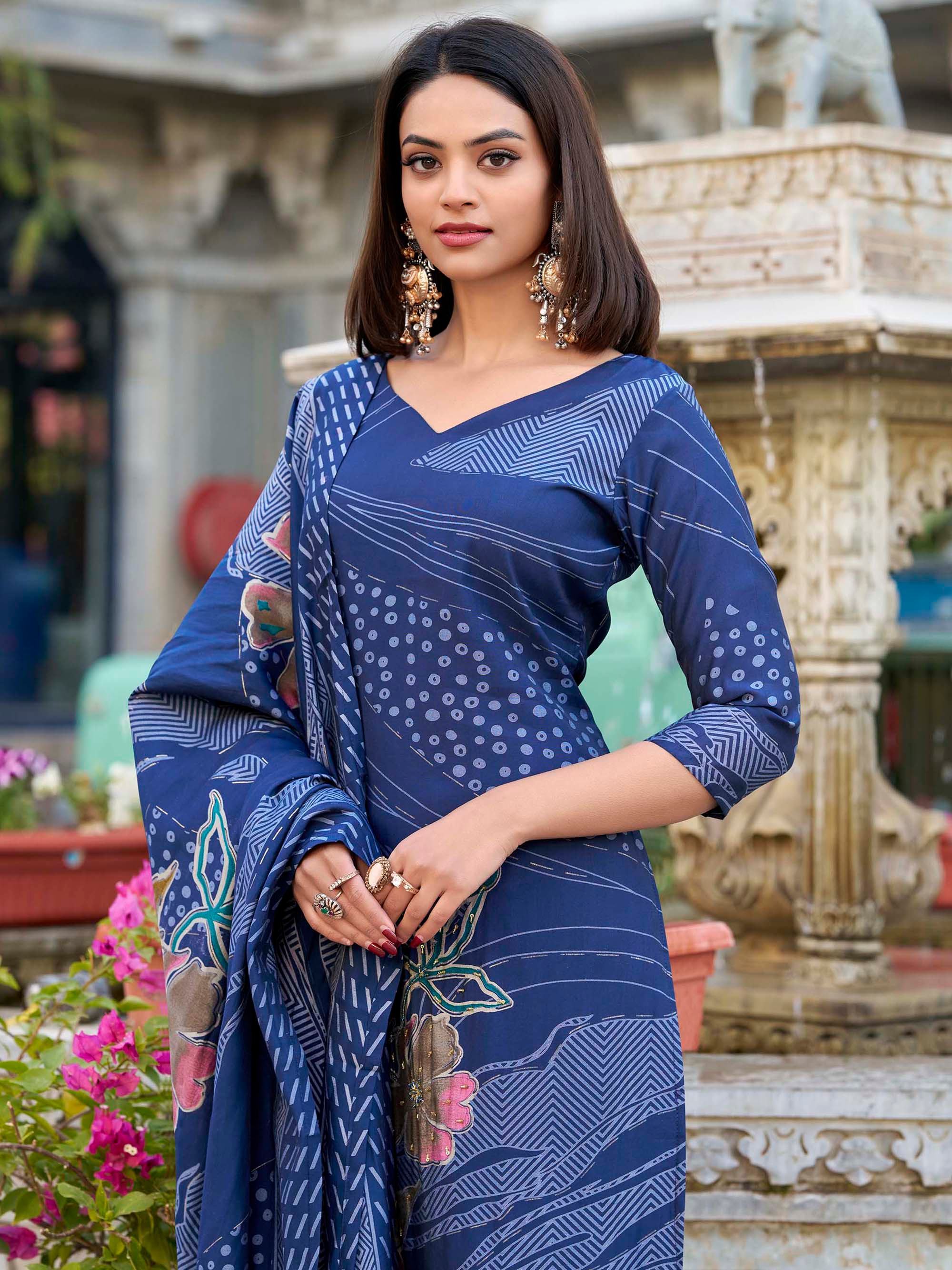Woman in blue printed saree with floral patterns, traditional jewelry, standing outdoors