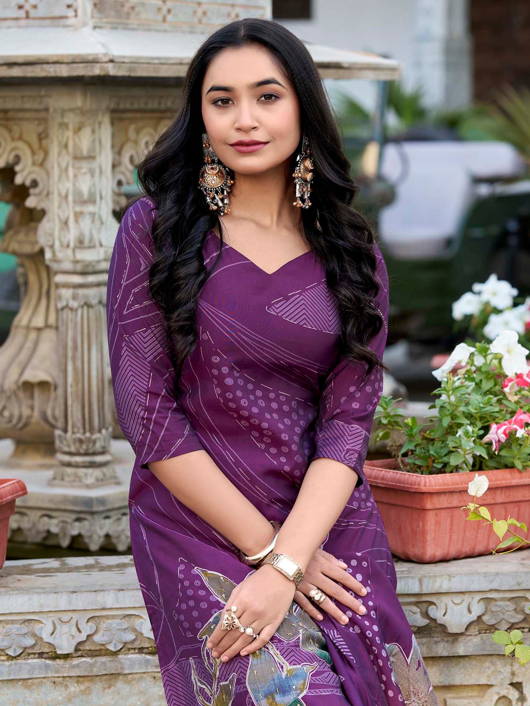 Woman in a purple ethnic saree with floral designs, wearing statement earrings outdoors