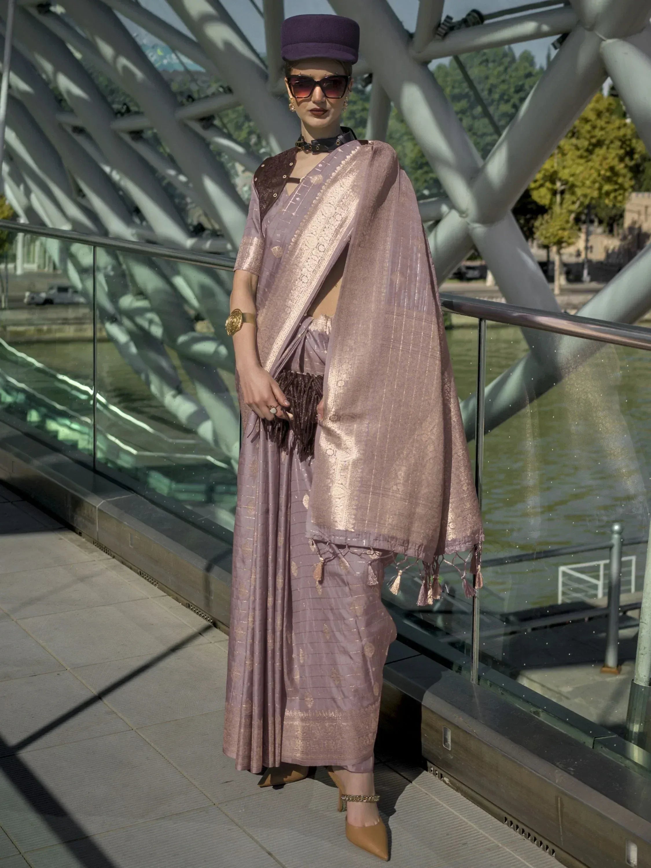 Elegant mauve saree with gold zari, modern blouse, and purple hat, styled on a bridge for ethnic fashion.