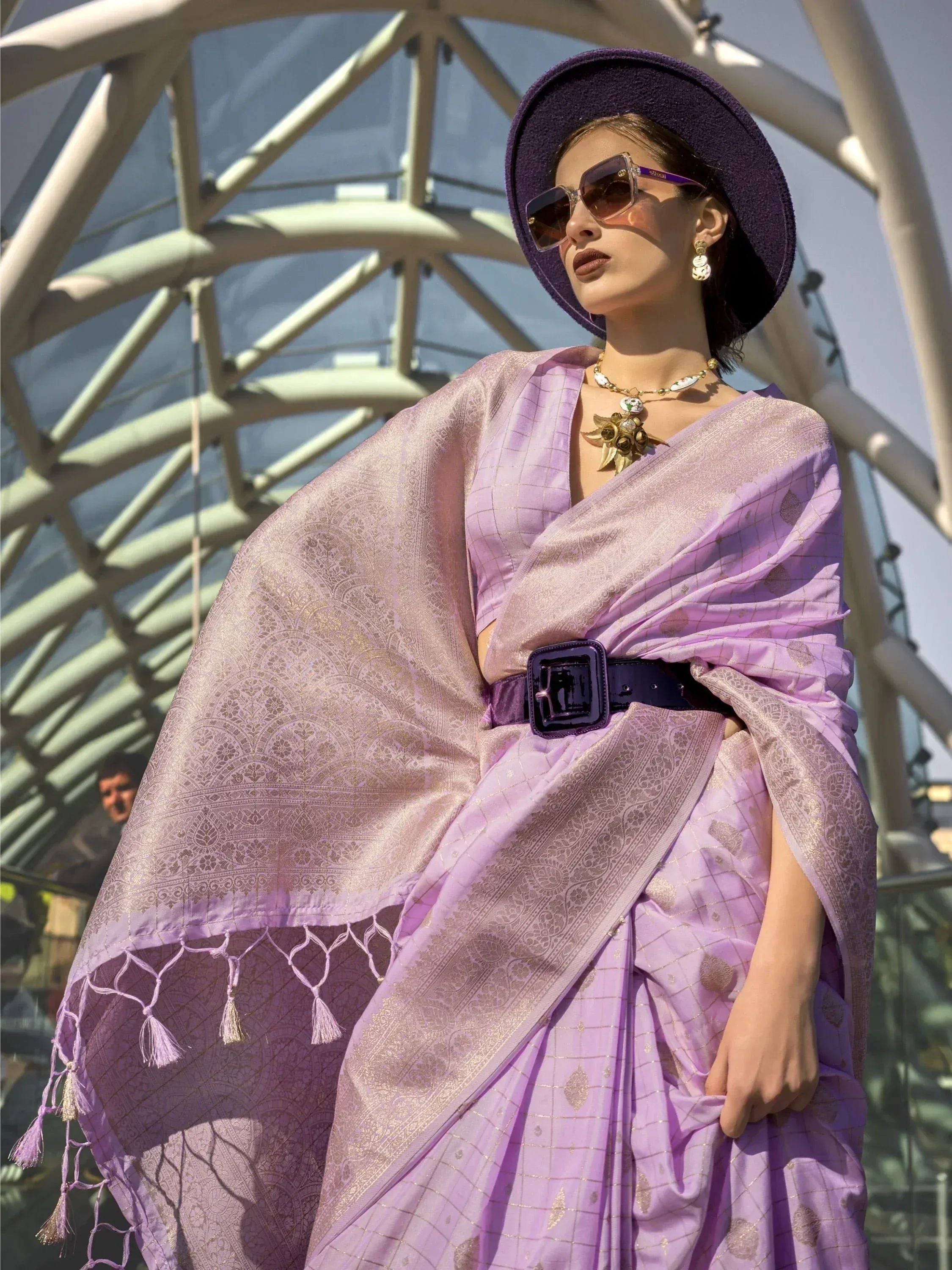 Lavender designer saree with gold weave, tassels, and belt, paired with purple hat and sunglasses