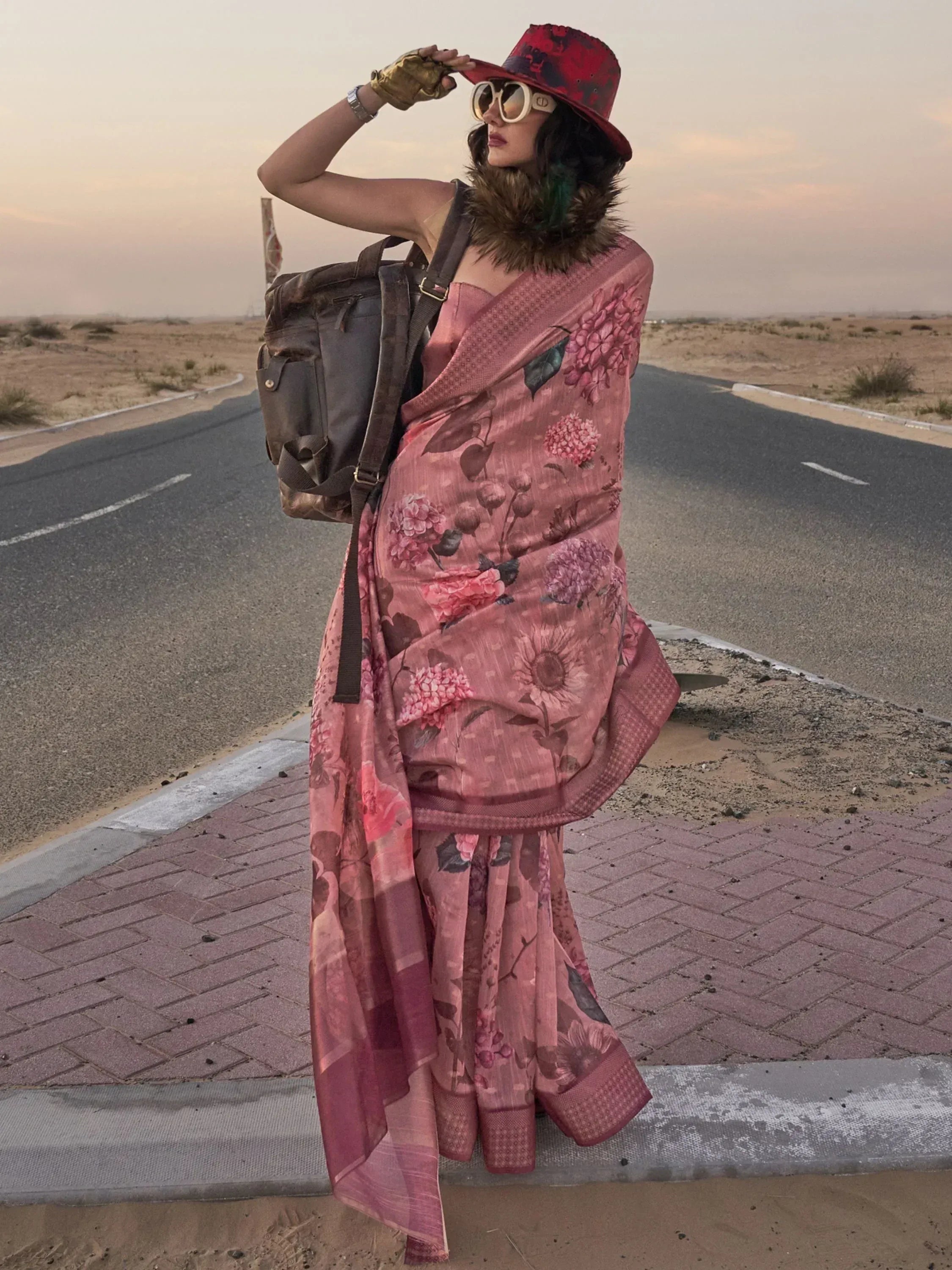 Woman in floral pink saree with red hat, desert road backdrop, ethnic fashion style