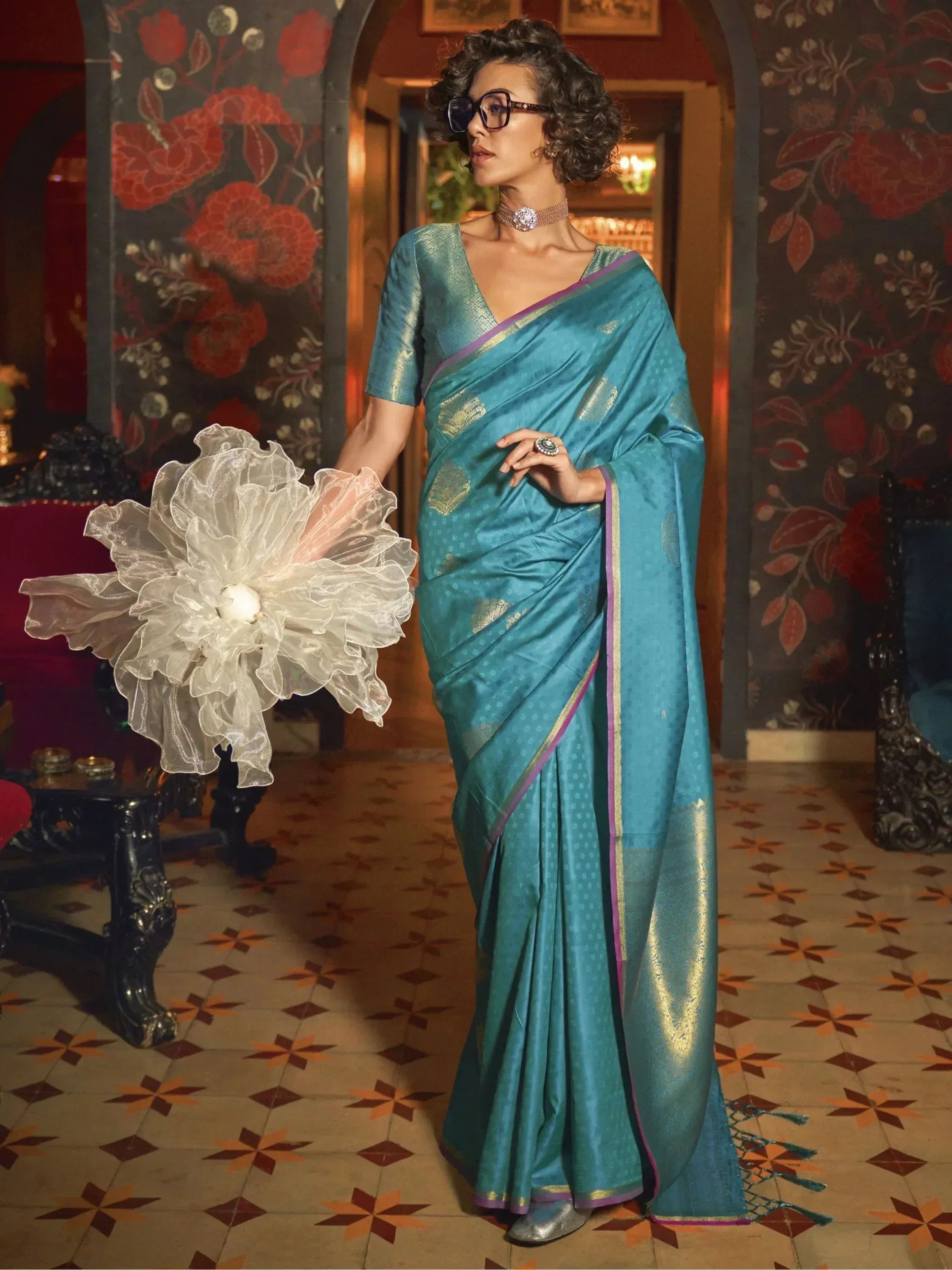 Elegant teal silk saree with gold motifs and purple border, styled with choker and statement ring for festive occasions