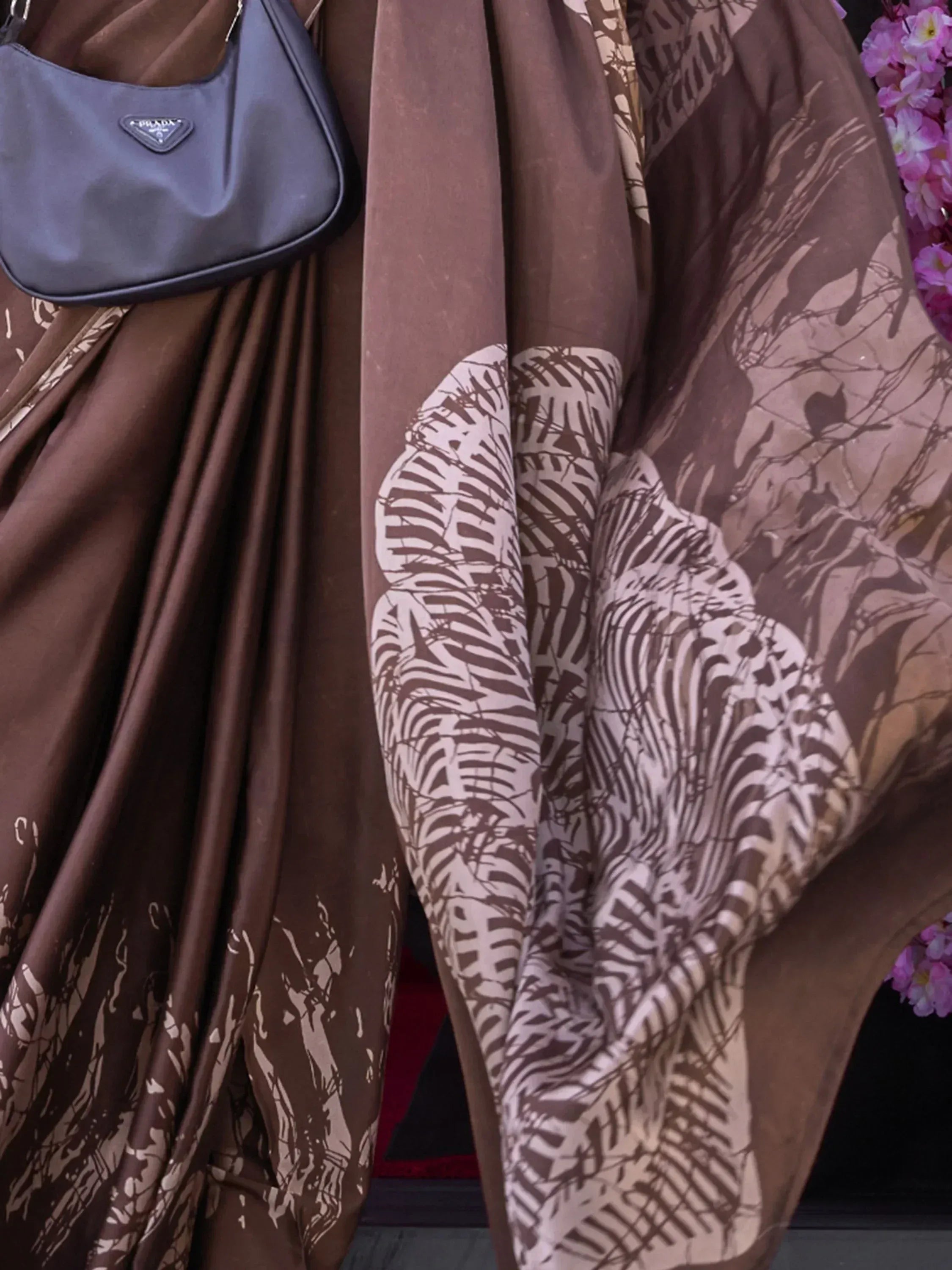 Brown printed ethnic gown with leaf pattern, paired with black handbag and pink flowers