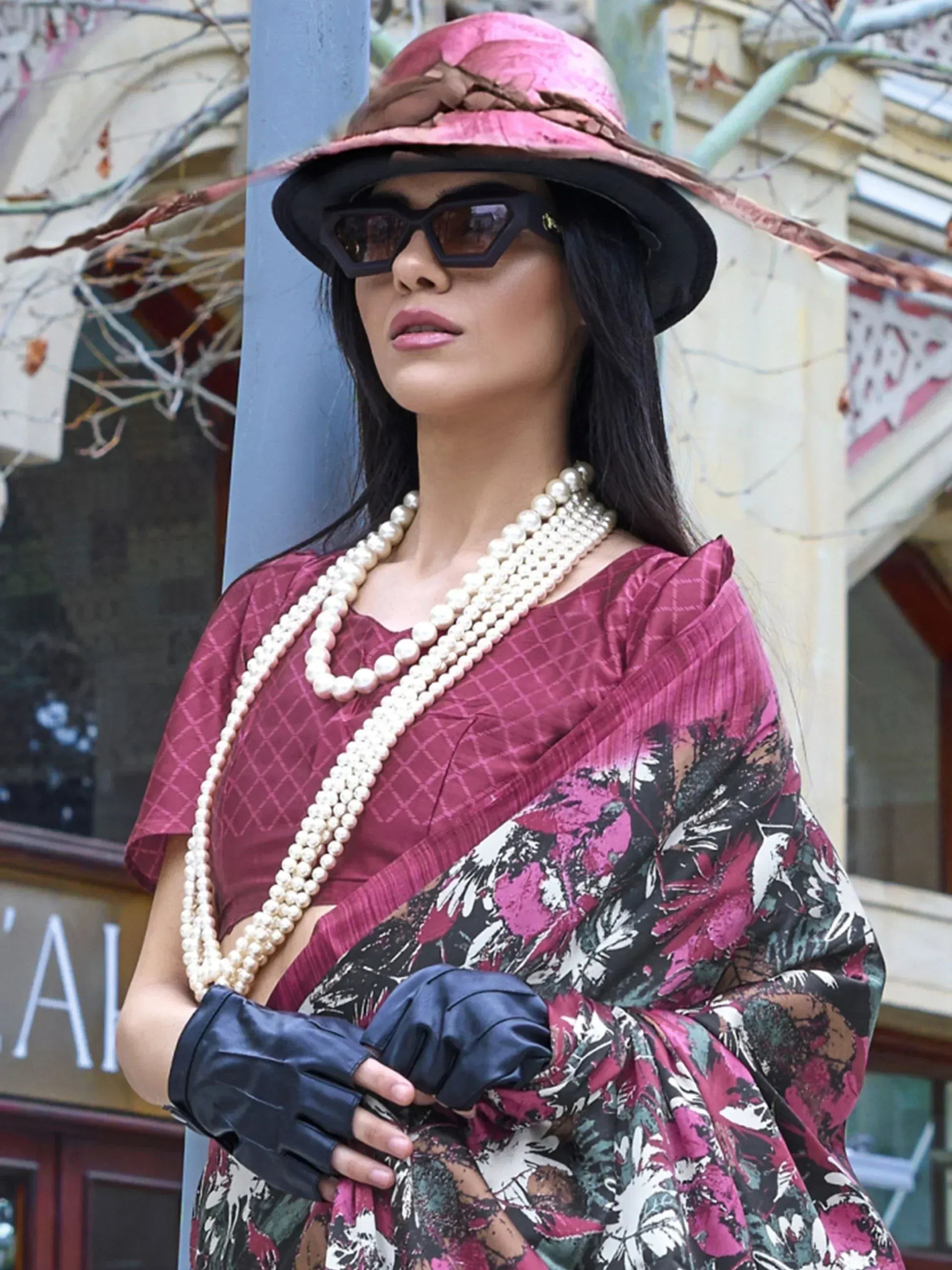 Woman in floral saree with pink hat, pearl necklace, and black gloves, styled for ethnic fashion