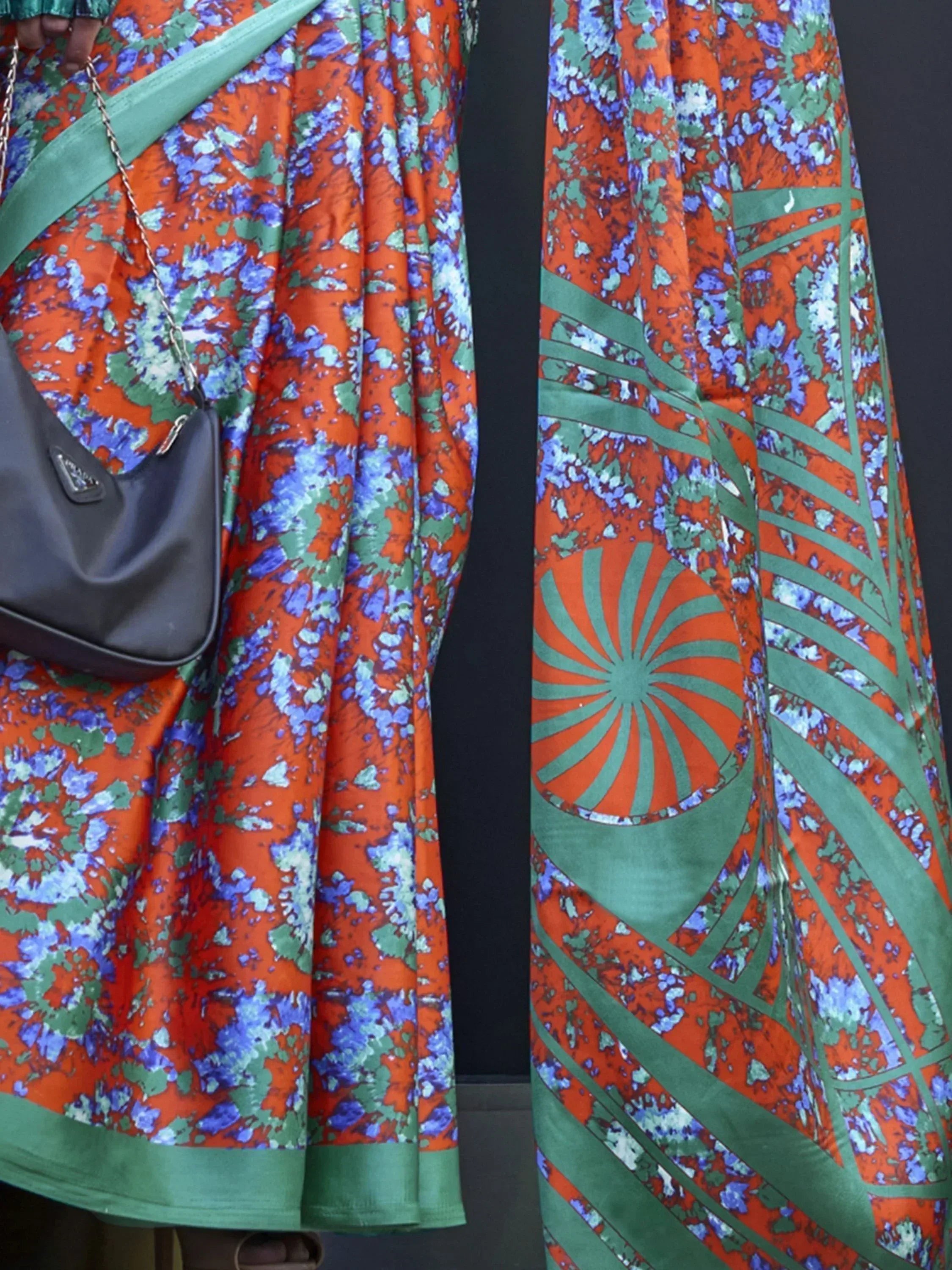 Vibrant orange, blue, and green floral printed ethnic gown with geometric border, styled with black handbag