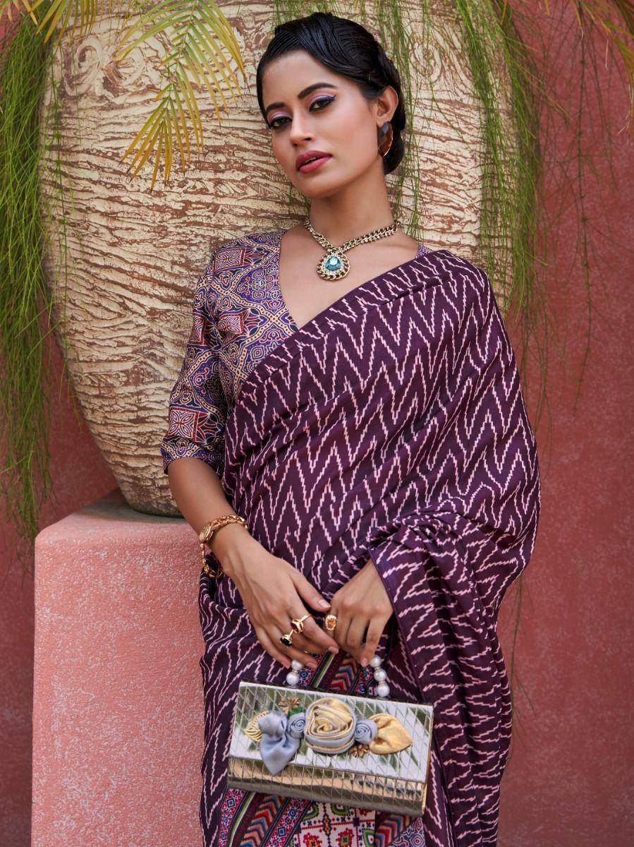 Woman in purple printed saree with ethnic jewelry and floral clutch, styled for Indian ethnic wear