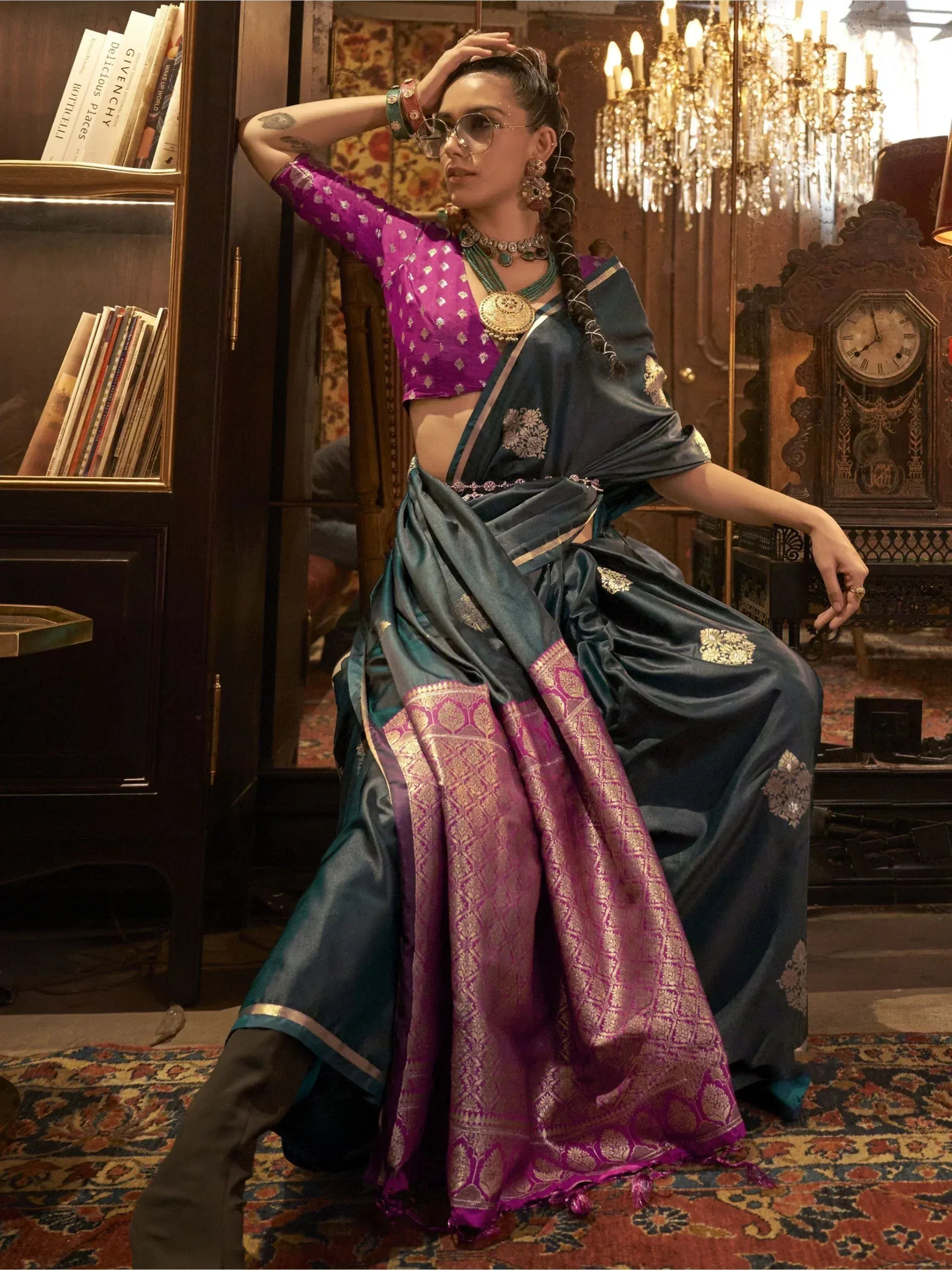 Woman in teal and purple designer saree with gold embroidery, styled with statement jewelry and sunglasses.