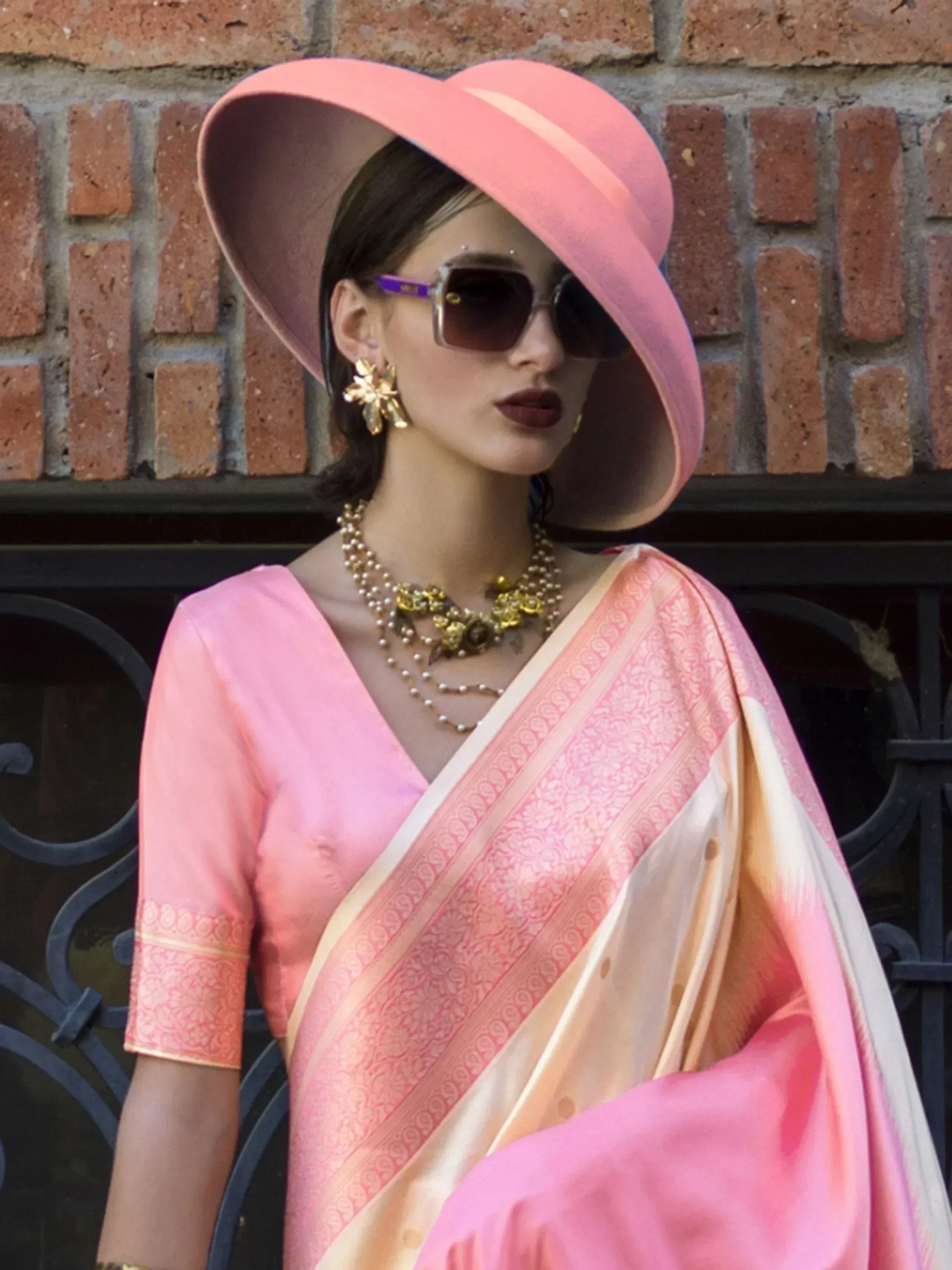 Pink ethnic saree with gold border, matching blouse, and wide-brim hat for festive occasions