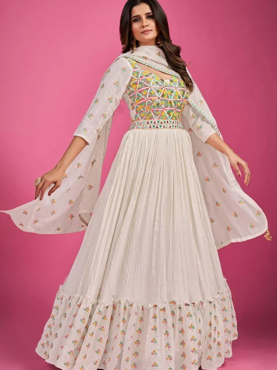 Woman wearing white embroidered ethnic gown with colorful geometric bodice, pink background