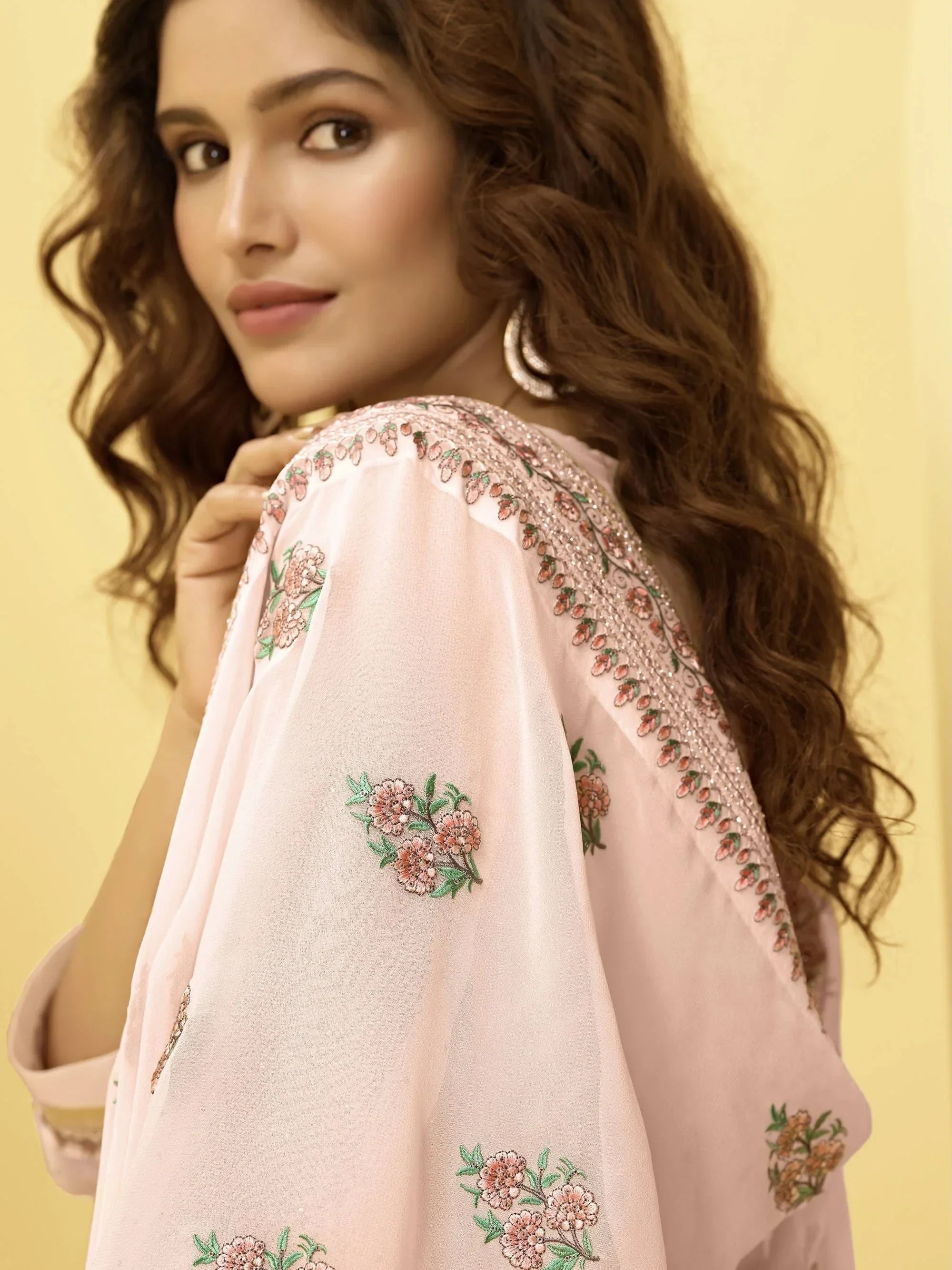 Woman in light pink embroidered ethnic saree with floral patterns and wavy hair