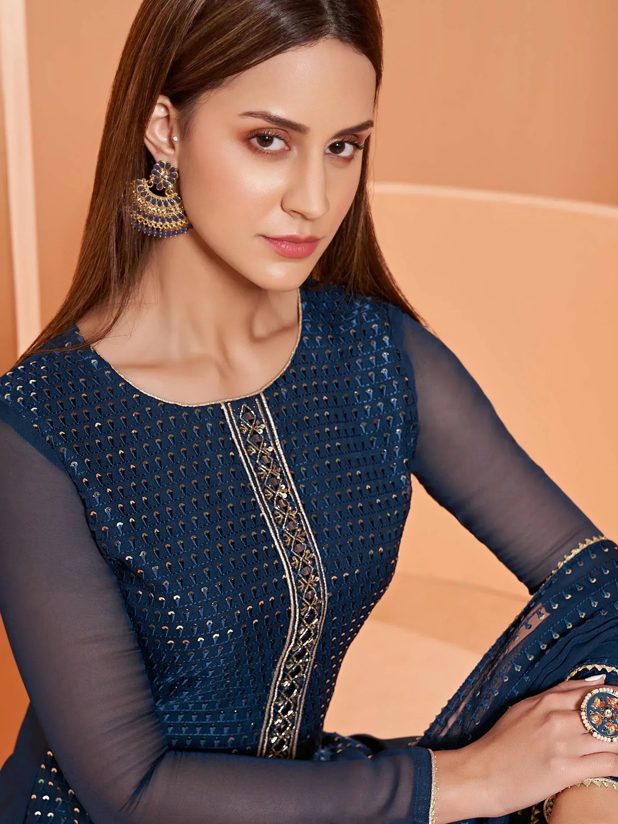 Woman in navy blue embroidered ethnic gown with sheer sleeves and gold detailing, paired with statement earrings.