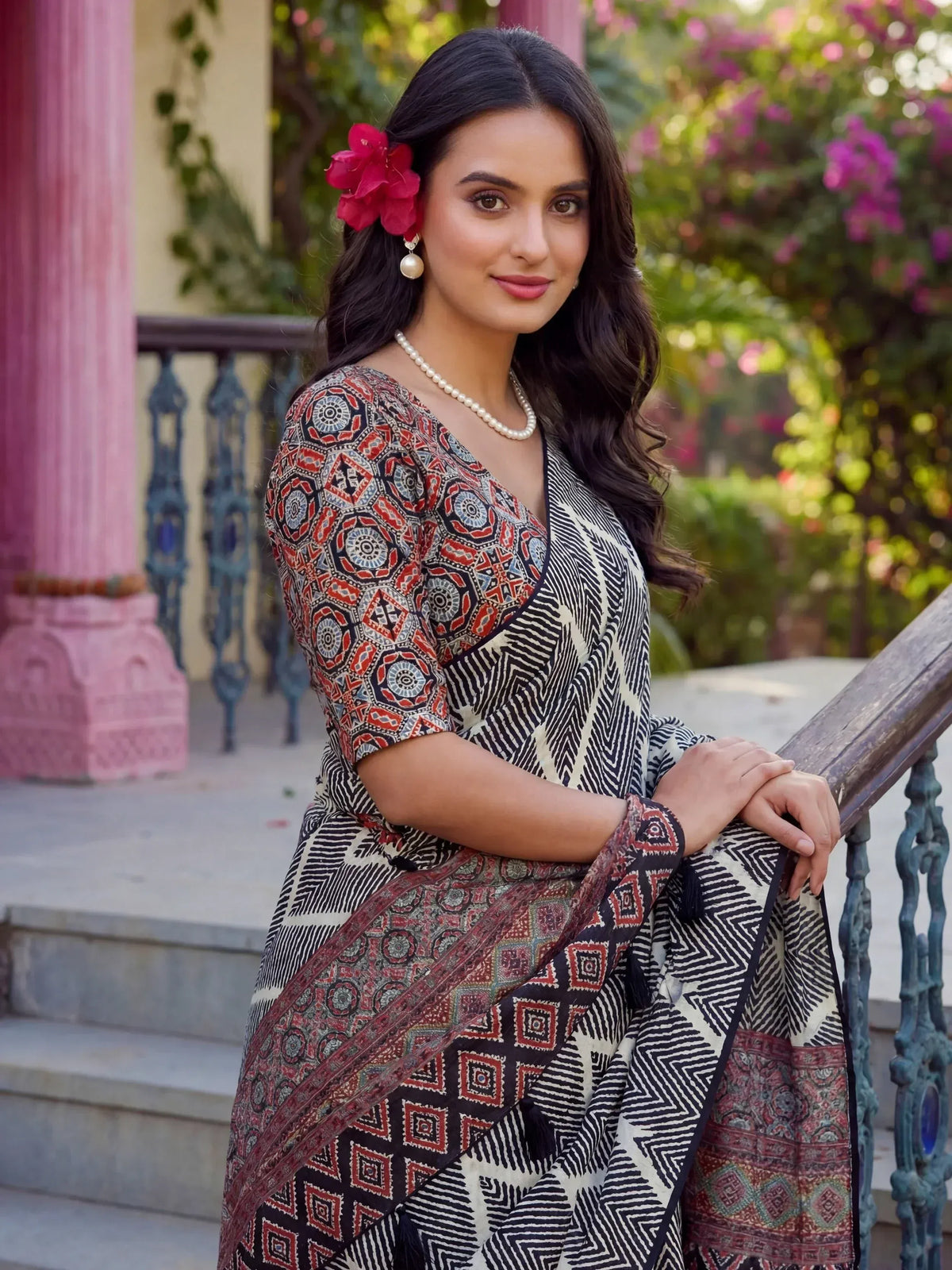 Woman in printed ethnic saree with geometric patterns, pearl necklace, and red flower hair accessory