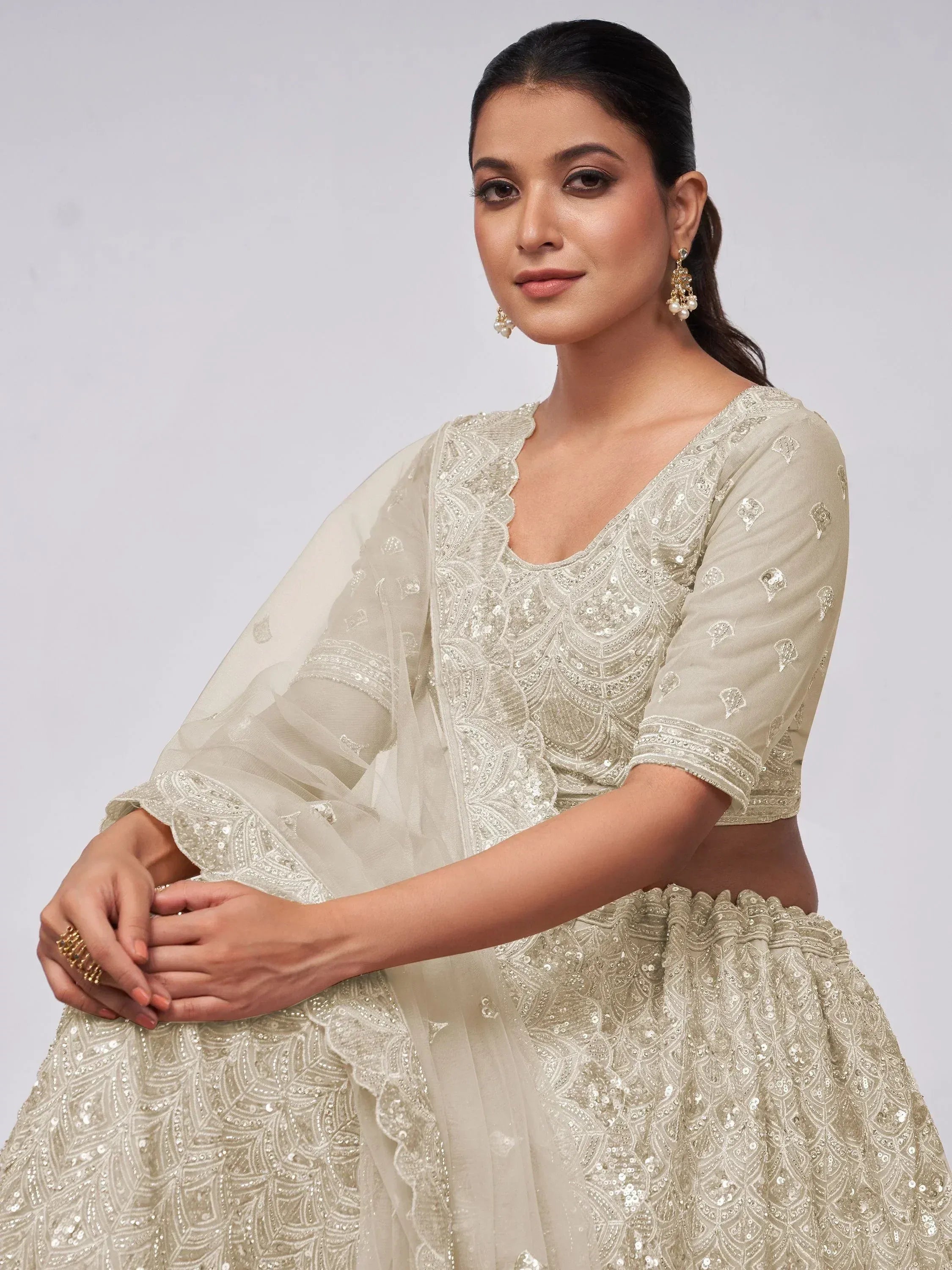Elegant cream lehenga choli with intricate sequin embroidery and sheer dupatta, perfect for Indian ethnic occasions.