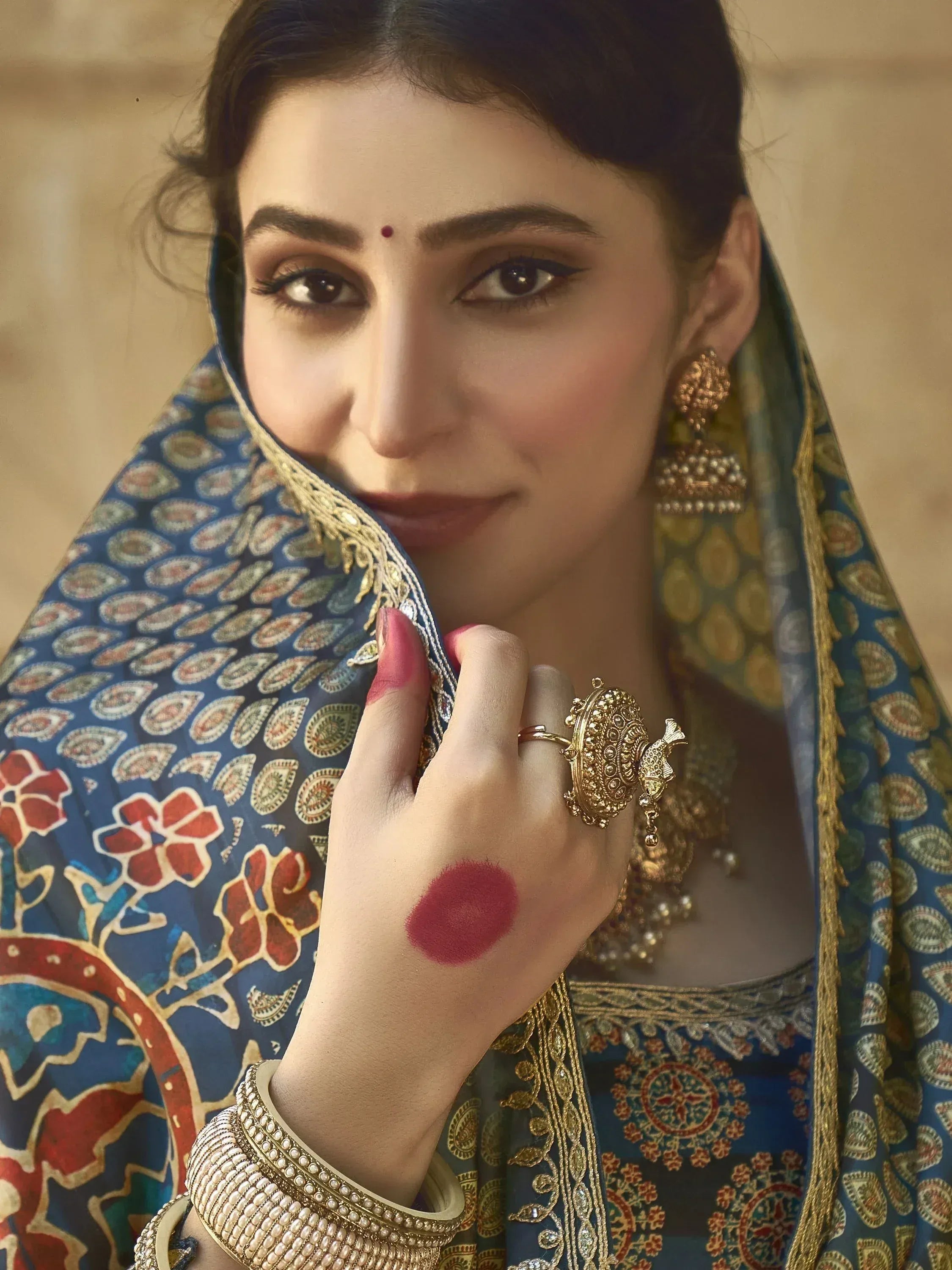 Woman in blue floral ethnic wear with gold jewelry and red henna, showcasing traditional Indian fashion.