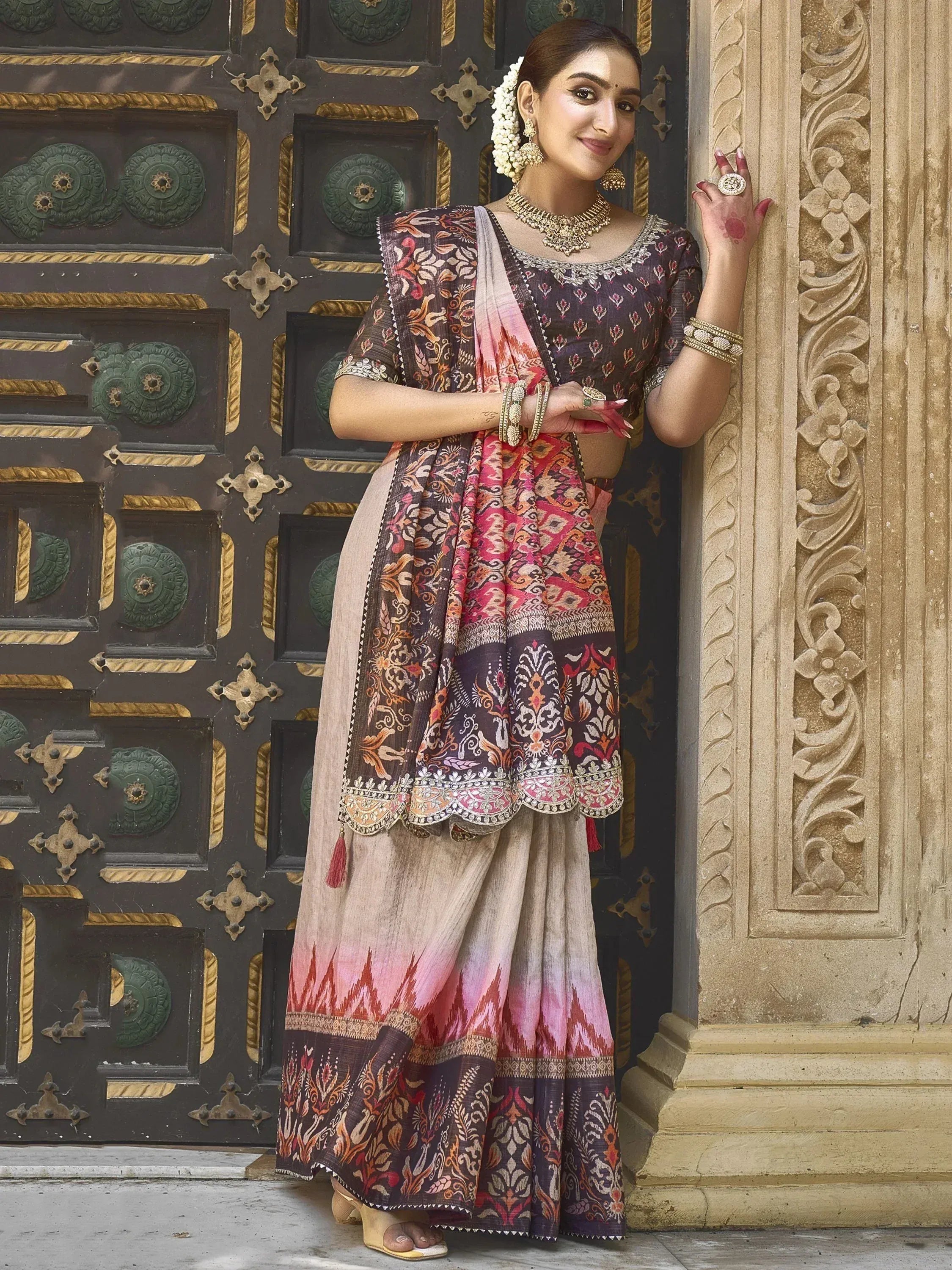 Woman in designer lehenga choli with floral print, gold jewelry, standing by ornate door