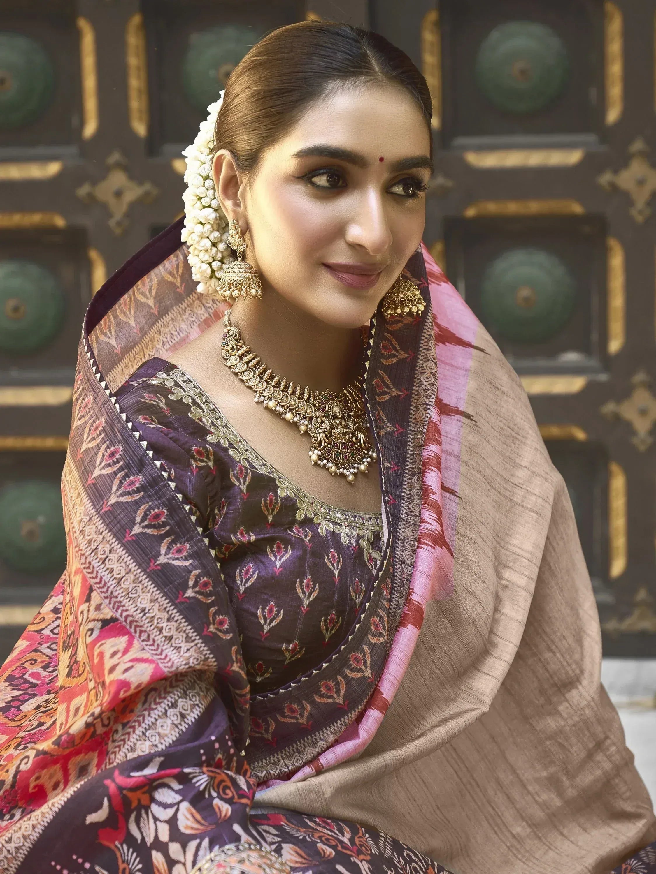 Woman in traditional Indian saree with floral print, gold jewelry, and jasmine hair accessory