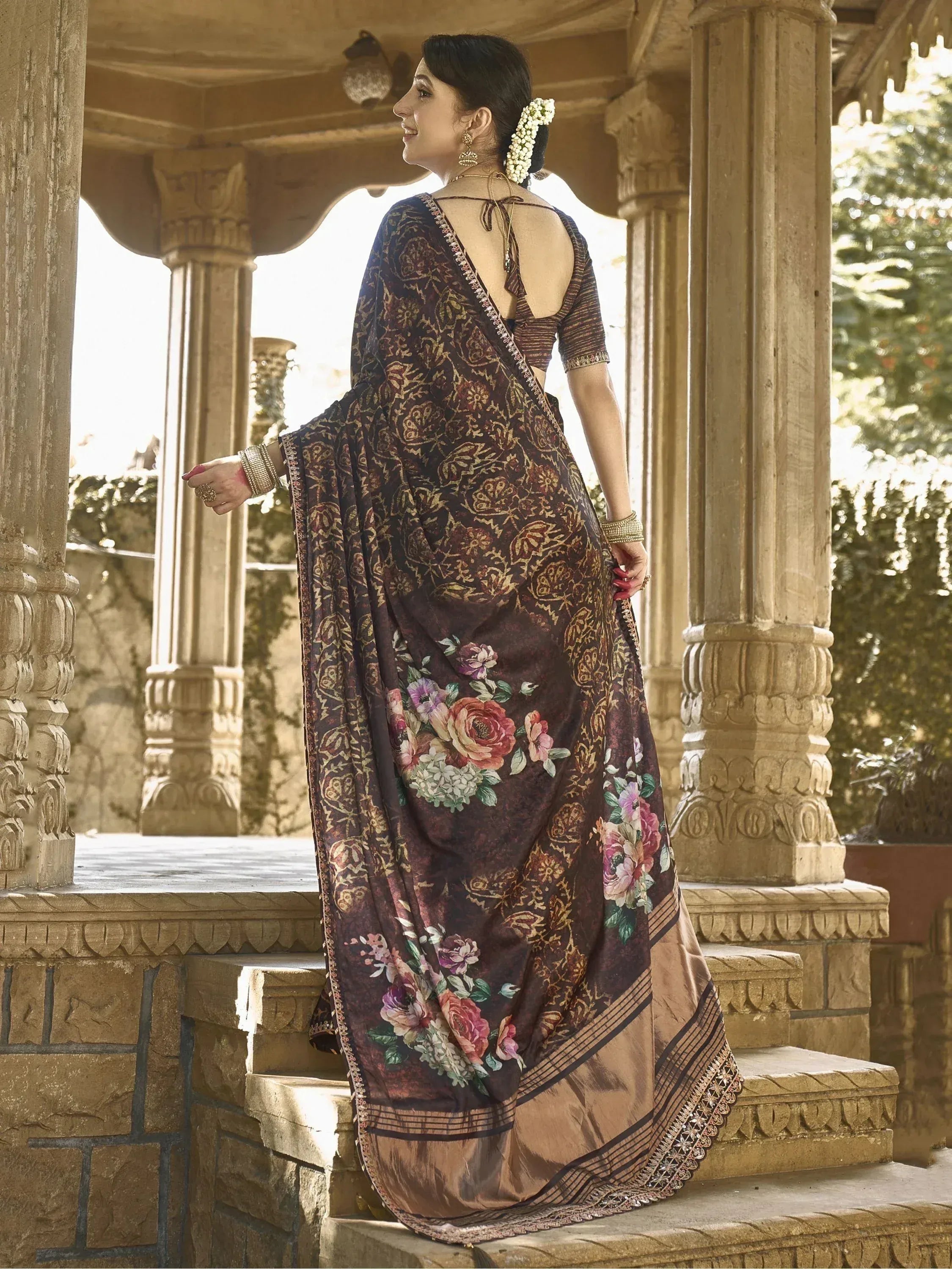 Woman in floral print ethnic saree with backless blouse, standing on stone steps