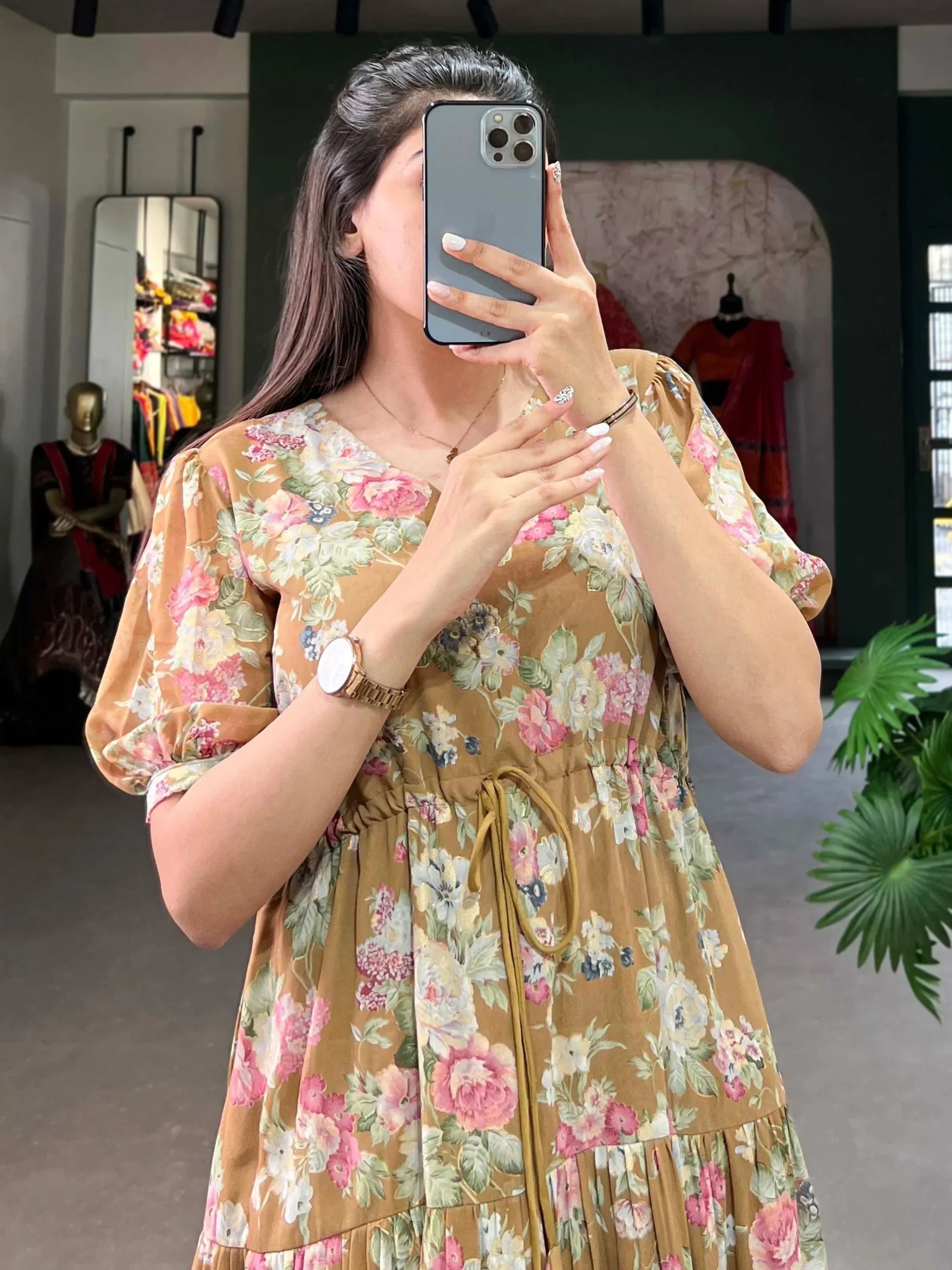 Woman wearing a brown floral print ethnic dress with puff sleeves, taking a mirror selfie in a boutique.