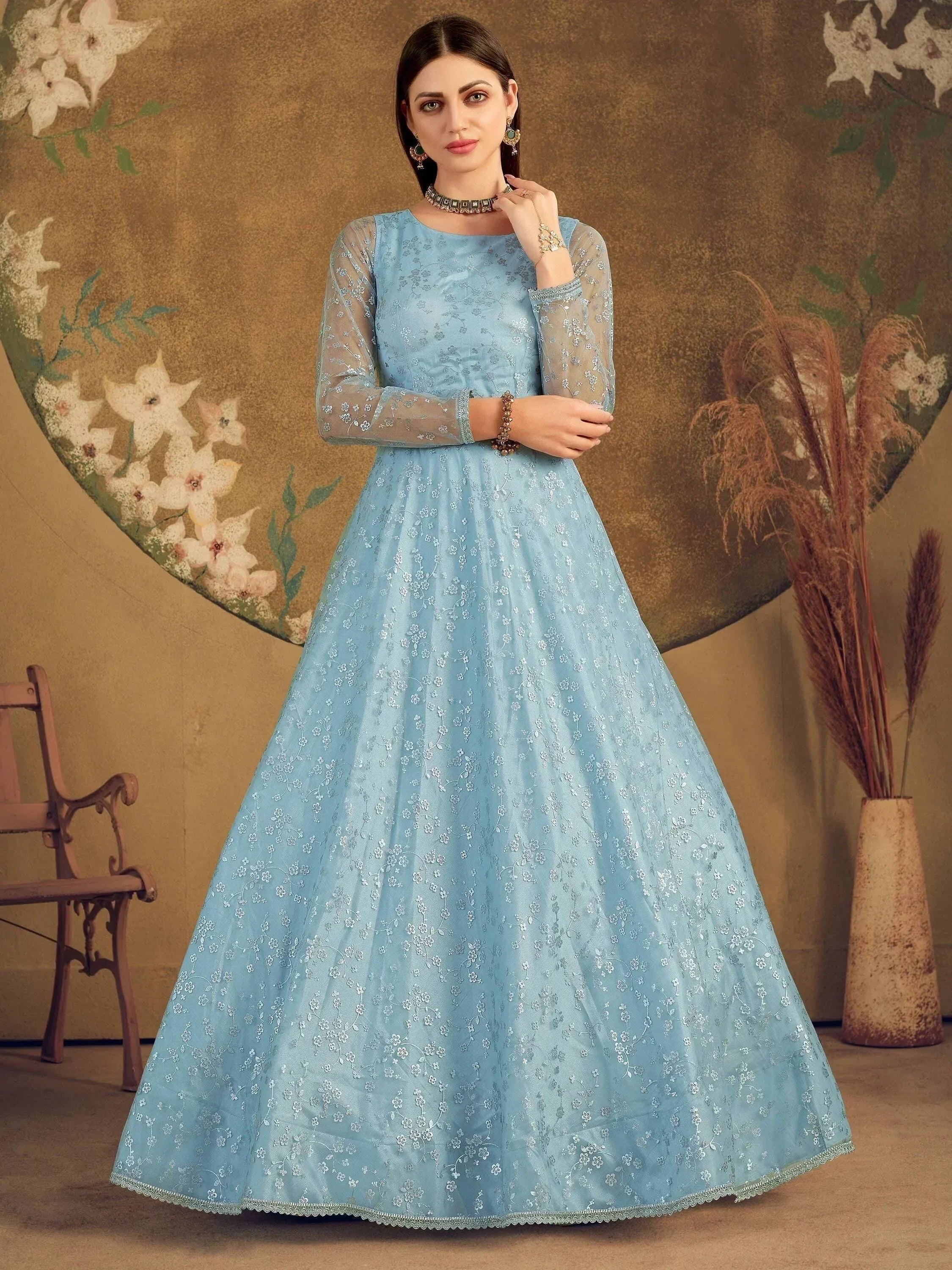 Woman wearing a light blue embroidered ethnic gown with sheer sleeves, floral backdrop