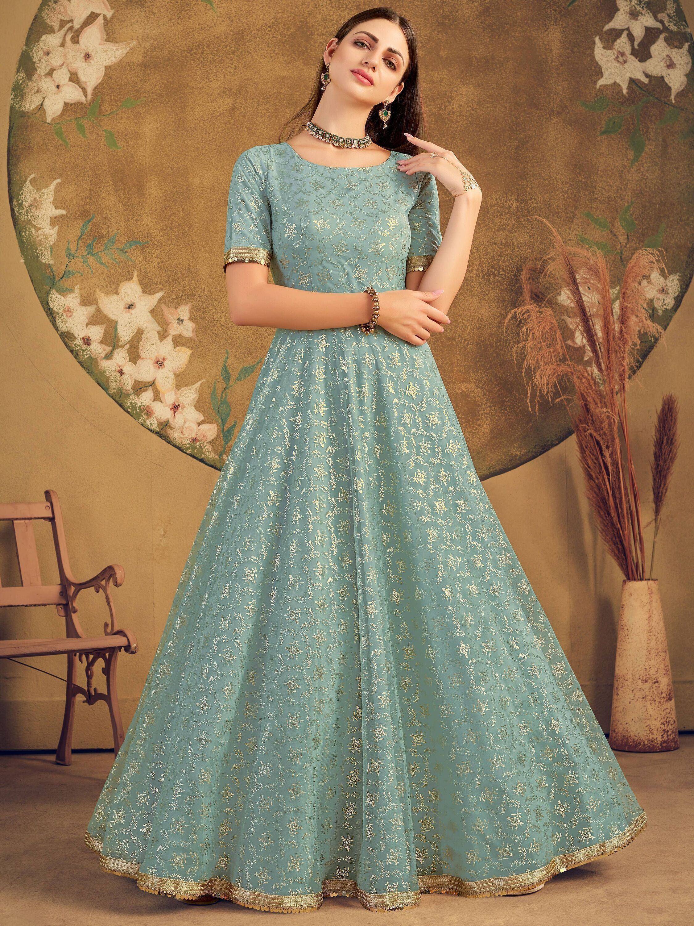 Woman wearing light blue ethnic gown with gold floral embroidery, standing indoors