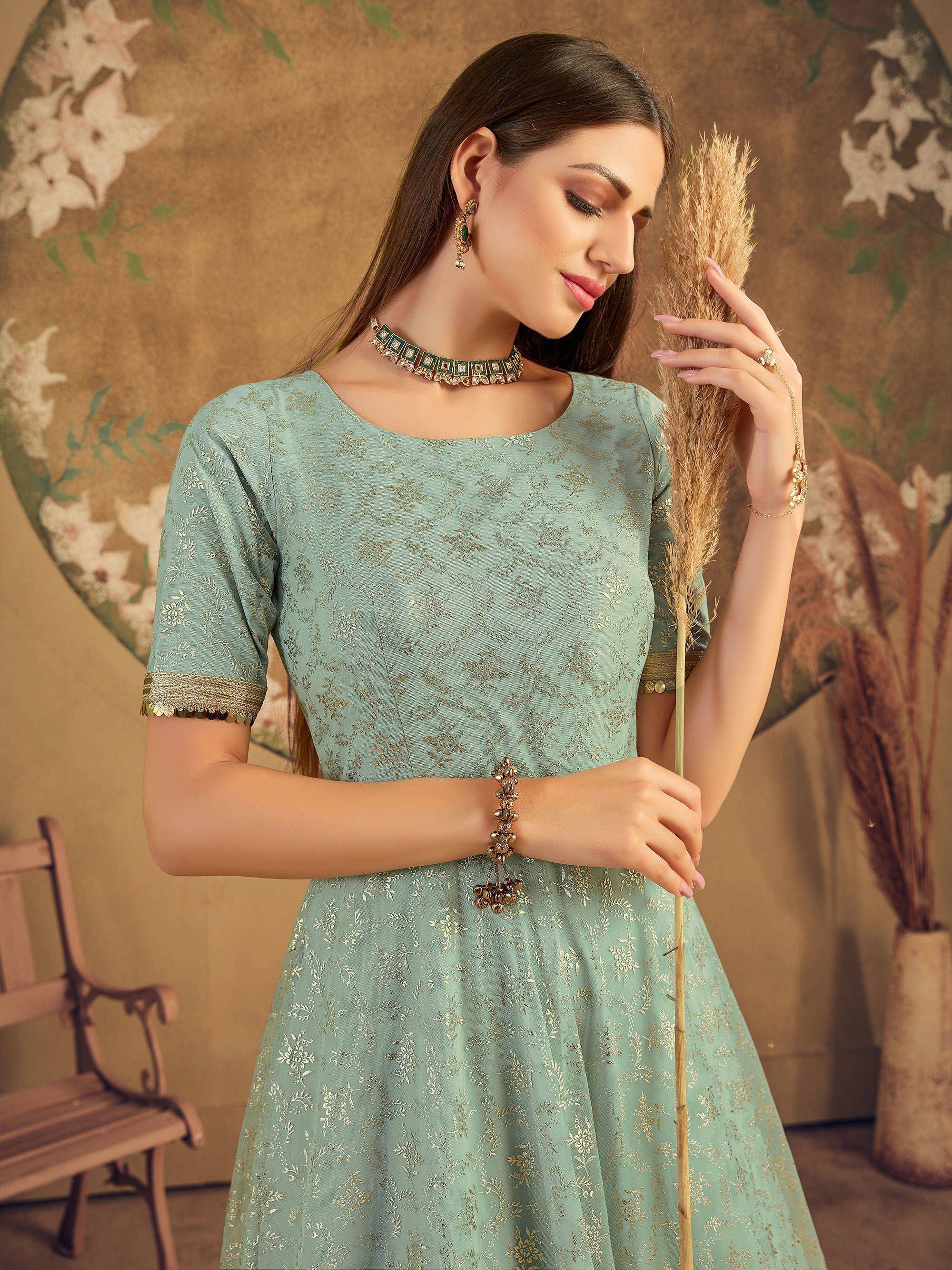 Woman in light blue embroidered ethnic gown with jewelry, floral background indoors