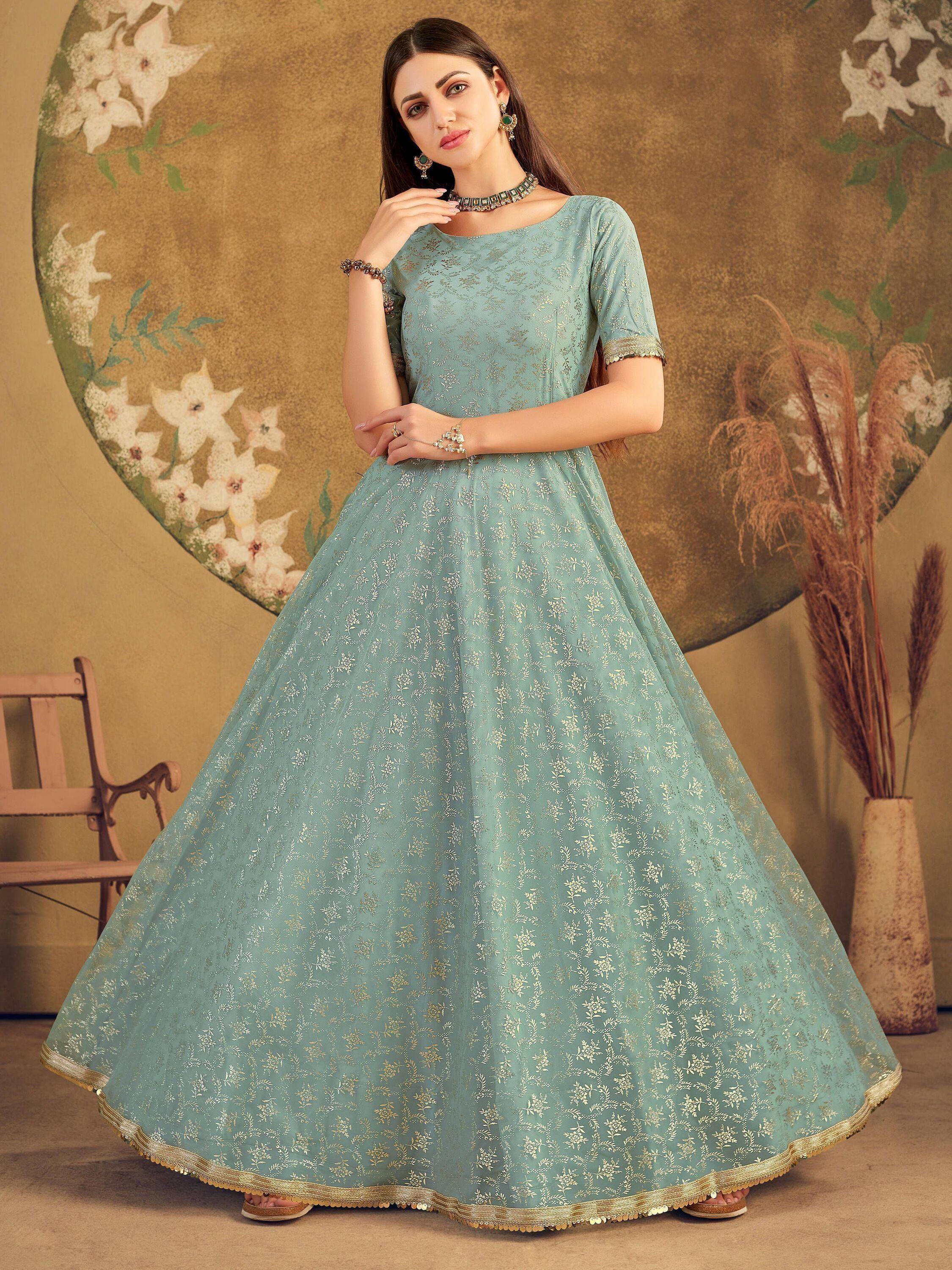 Woman wearing a light blue embroidered ethnic gown with gold detailing, floral backdrop