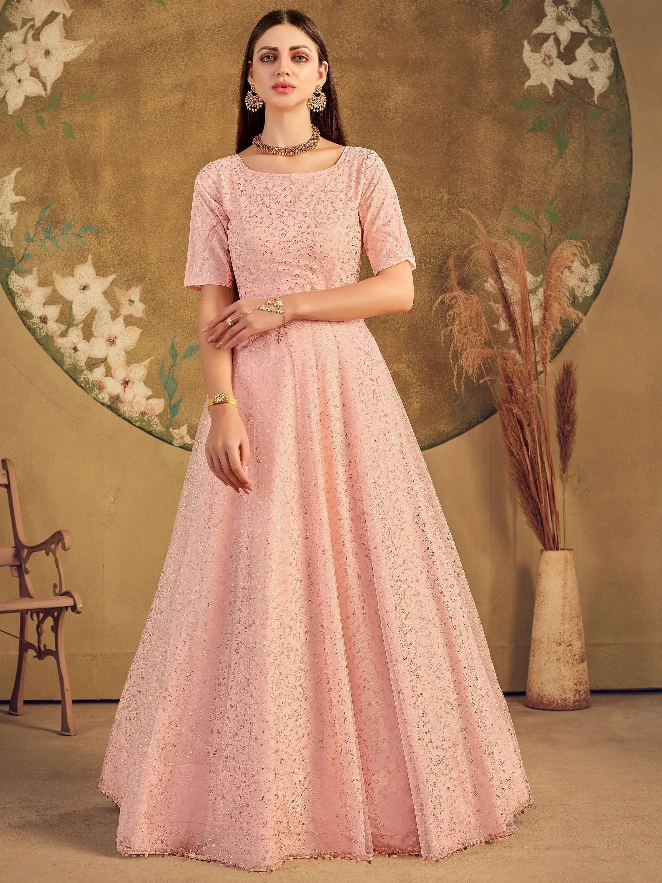 Pink embroidered ethnic gown with floral backdrop, perfect for Indian occasions and festive wear.