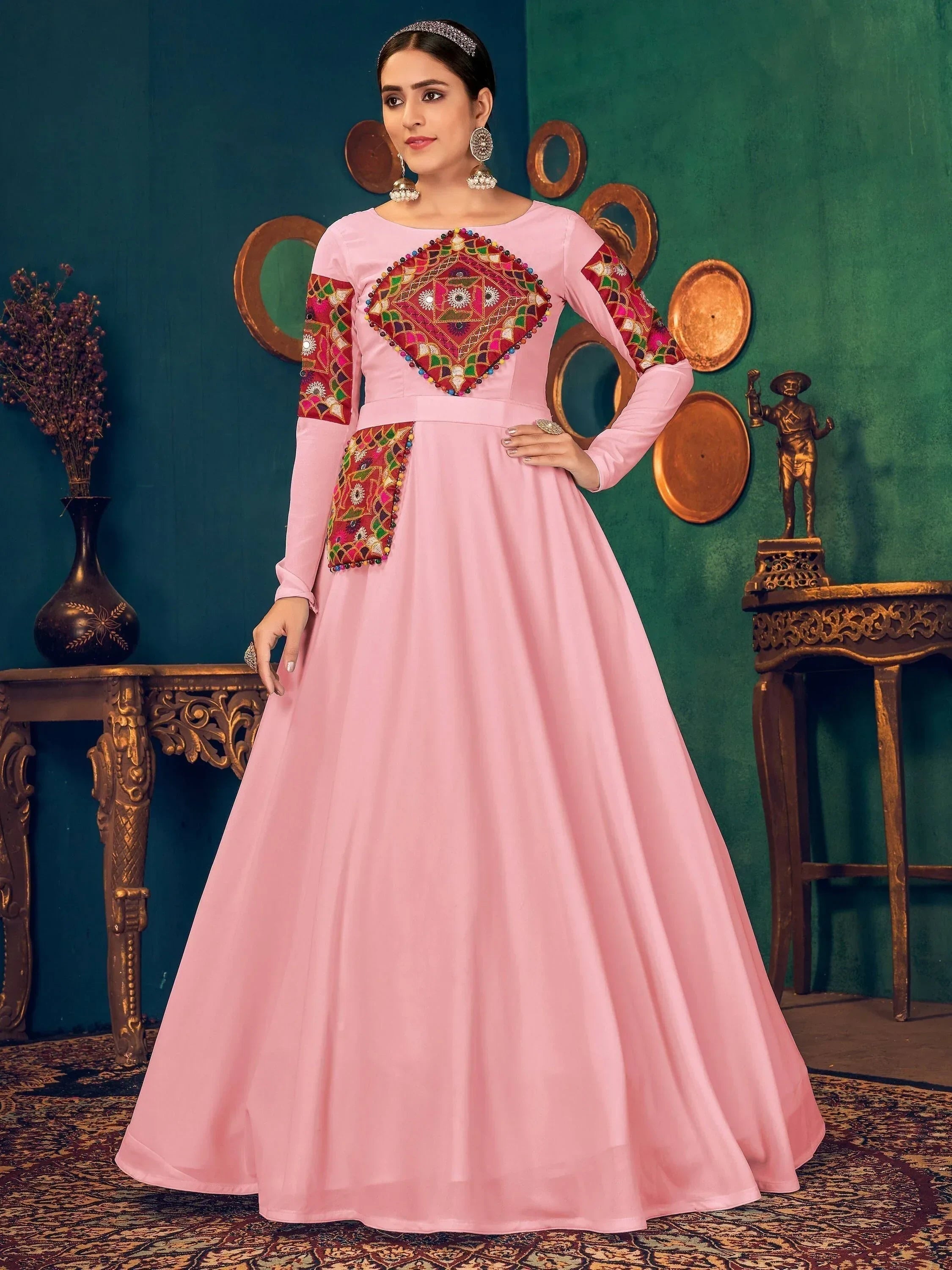 Woman wearing pink embroidered ethnic gown with long sleeves, standing in elegant room.