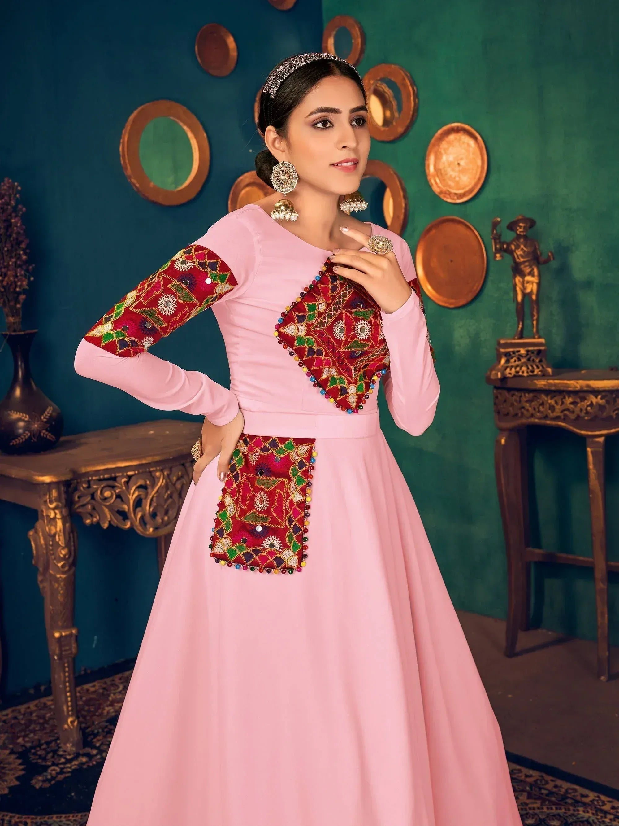 Pink ethnic gown with red embroidered panels and mirror work, styled with traditional jewelry for festive occasions