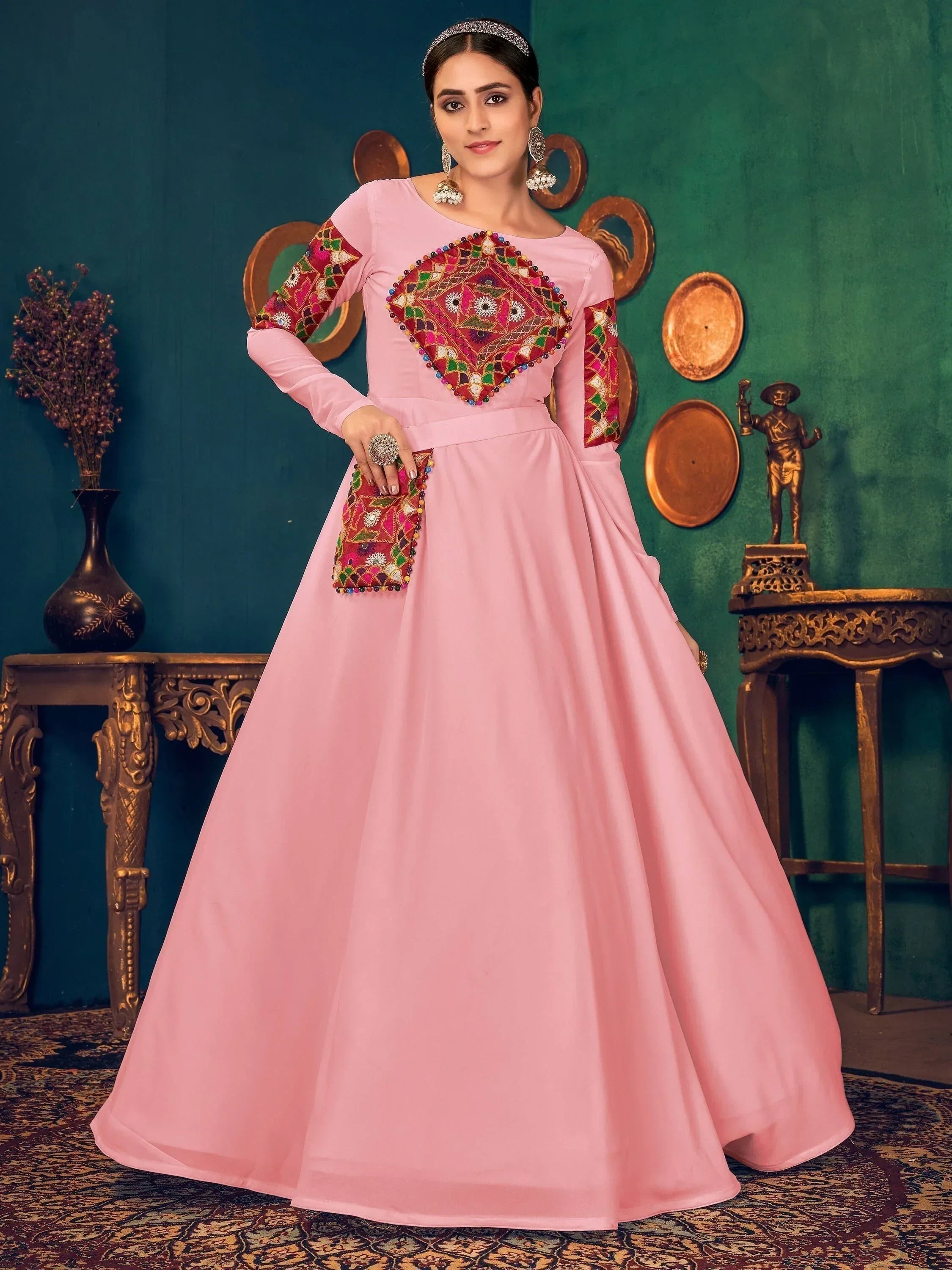 Woman in a pink ethnic gown with colorful embroidery and long sleeves, traditional decor background