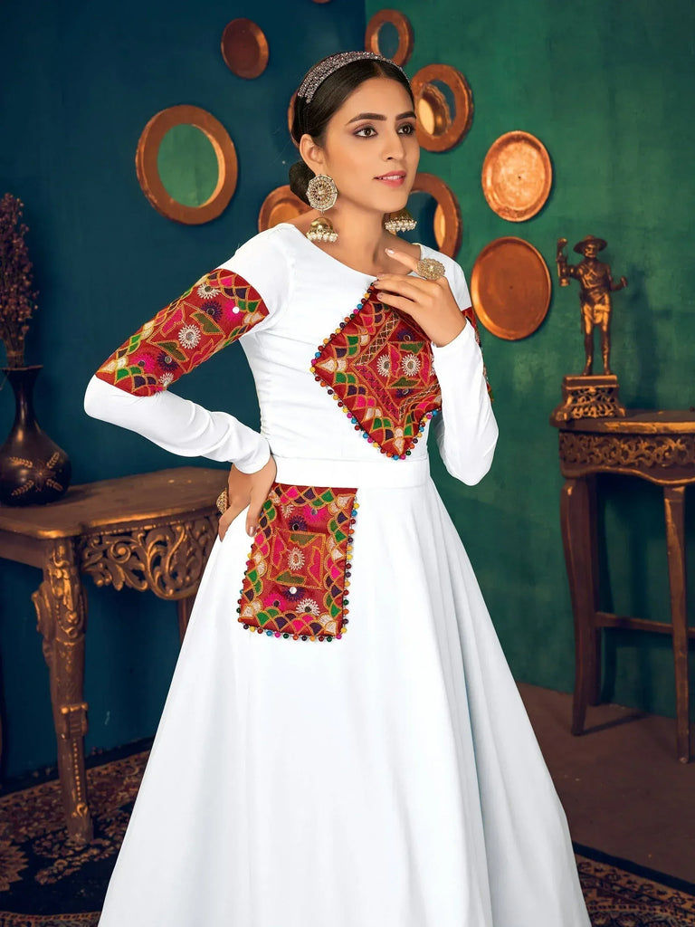 White ethnic gown with colorful embroidered panels and mirror work, styled with traditional jewelry