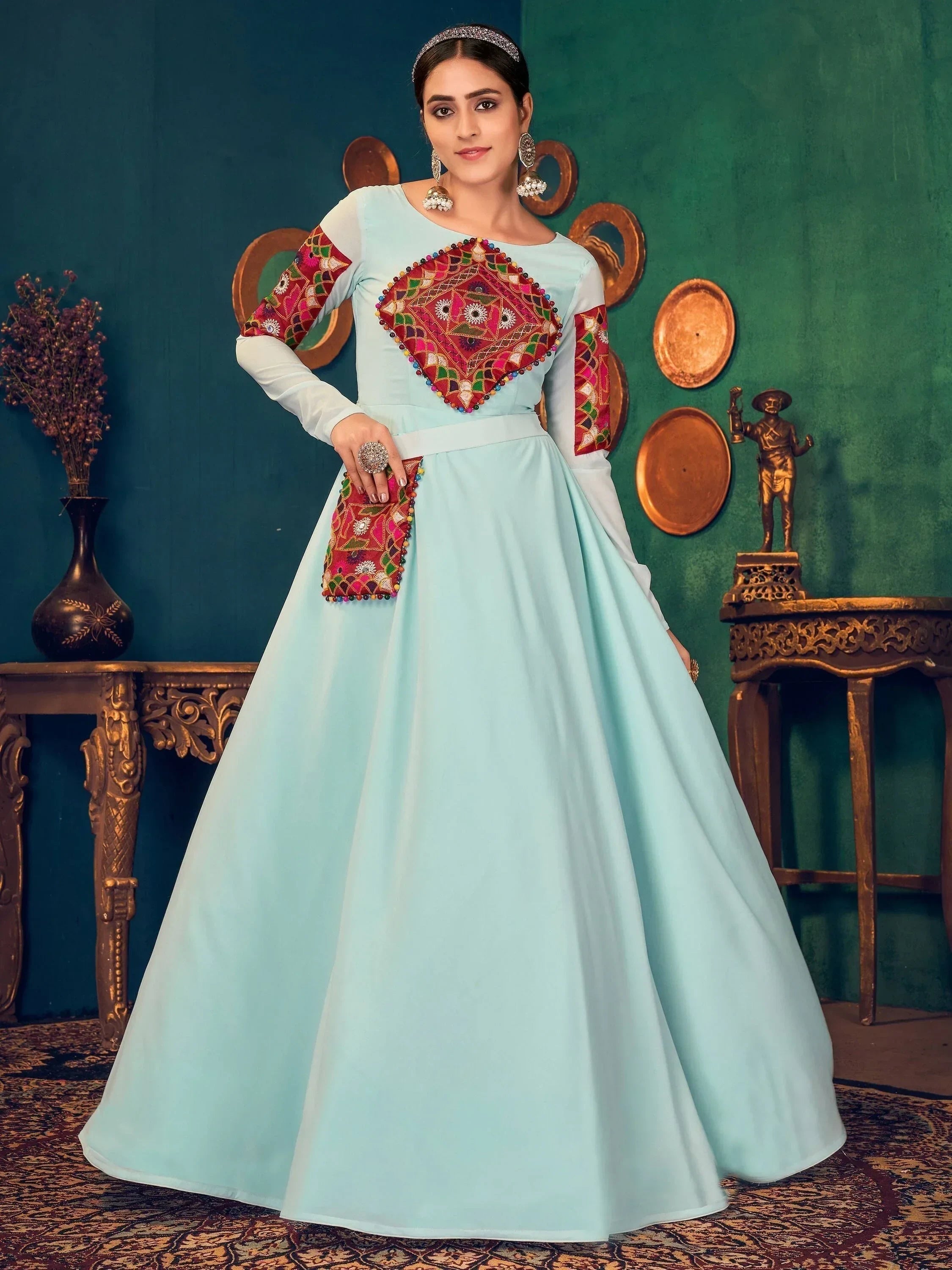 Woman in a light blue ethnic gown with vibrant multicolor embroidery, traditional decor backdrop