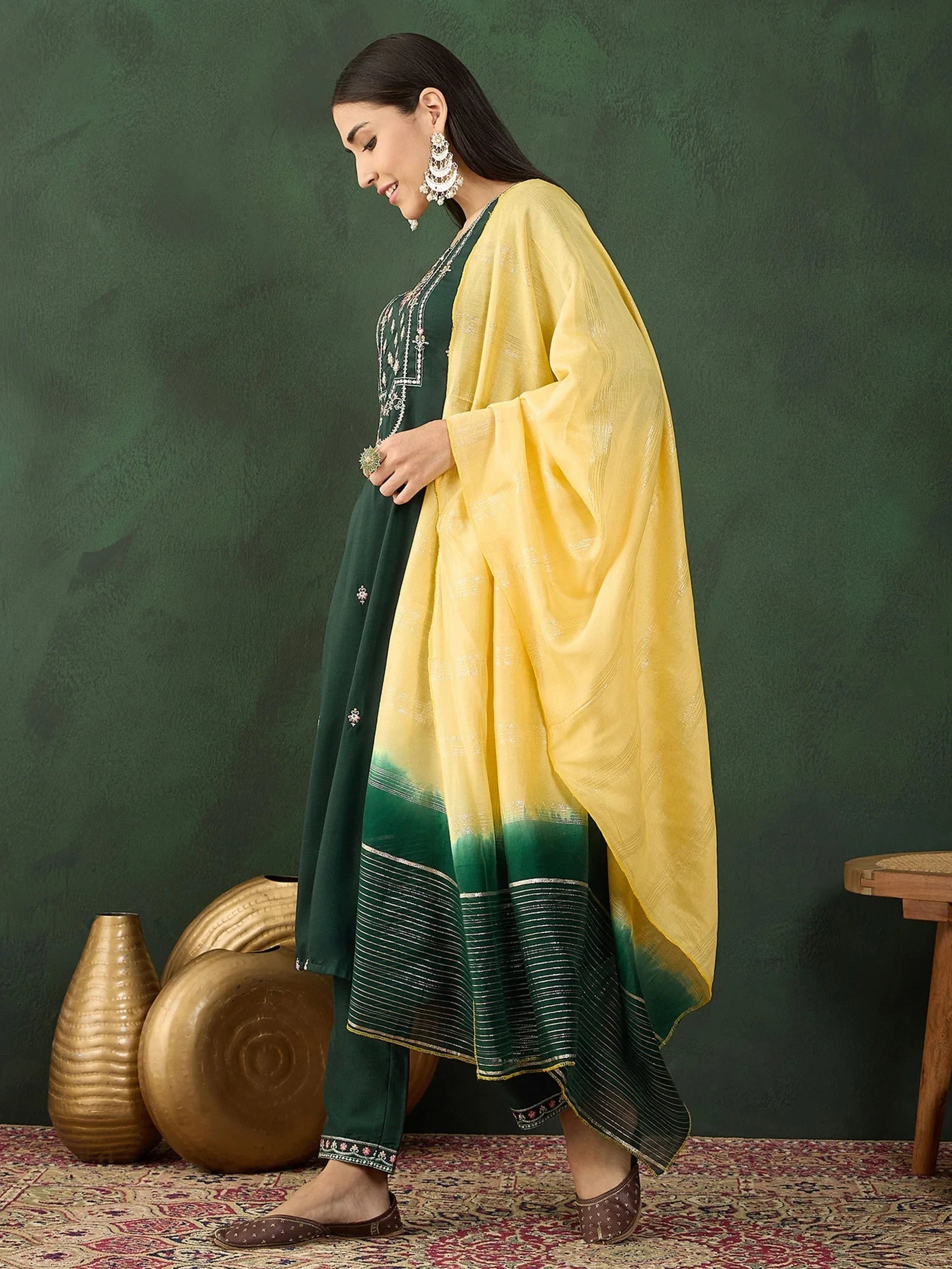 Woman in green salwar kameez with yellow dupatta, ethnic jewelry, indoor traditional setting