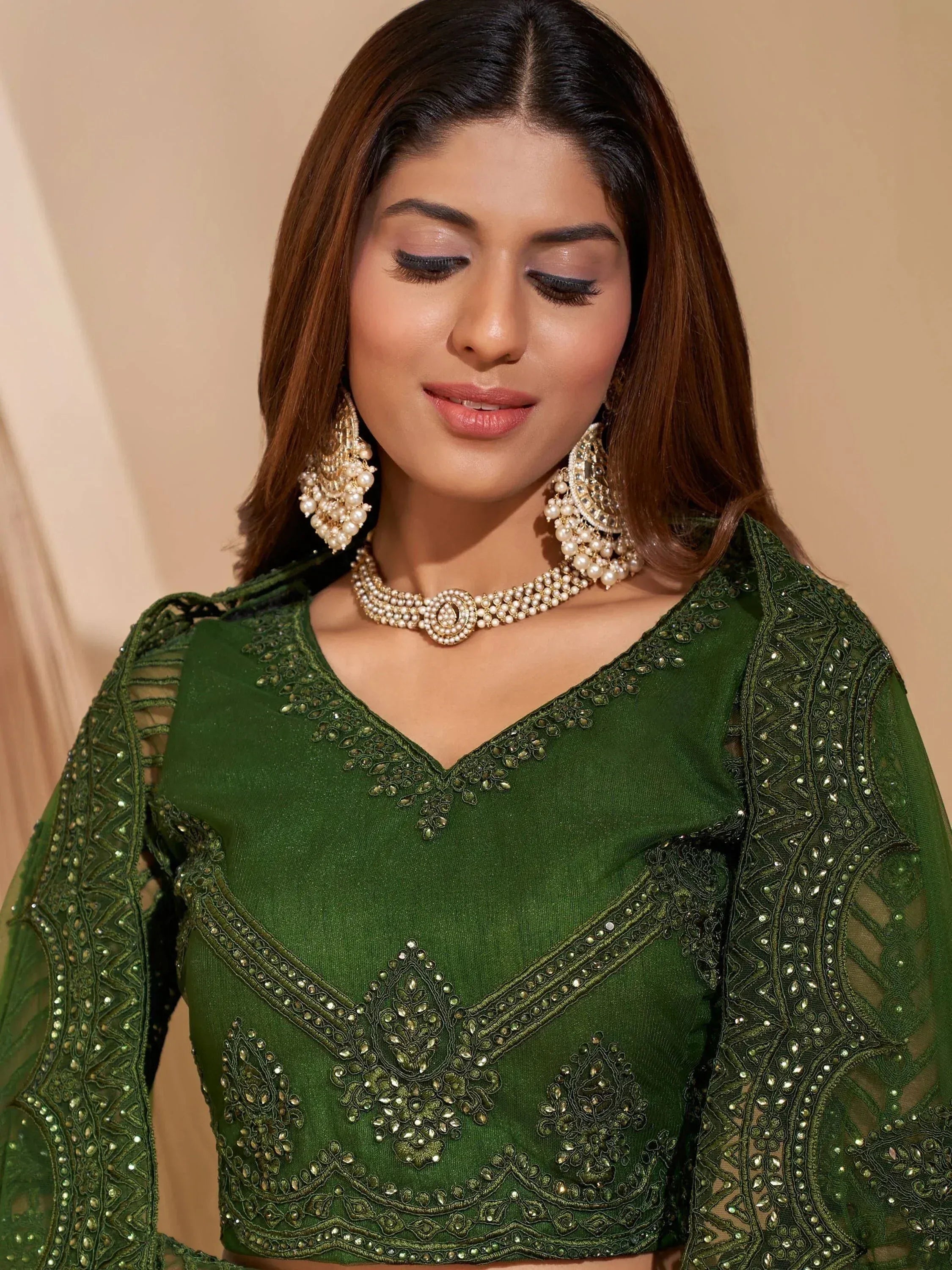 Emerald green embroidered lehenga choli with sheer sleeves and pearl jewelry, perfect for Indian ethnic wear.