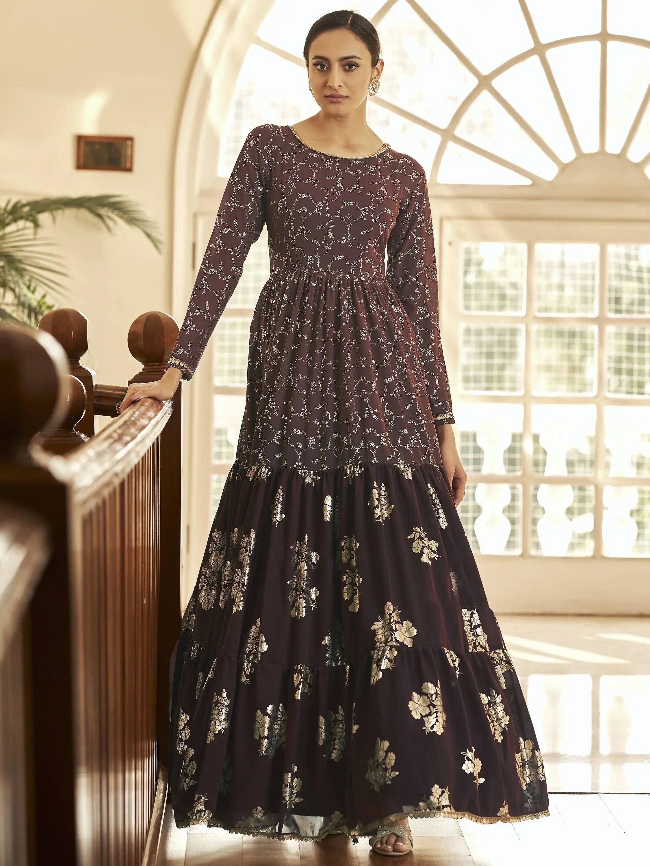 Woman in maroon ethnic gown with gold floral prints and long sleeves indoors