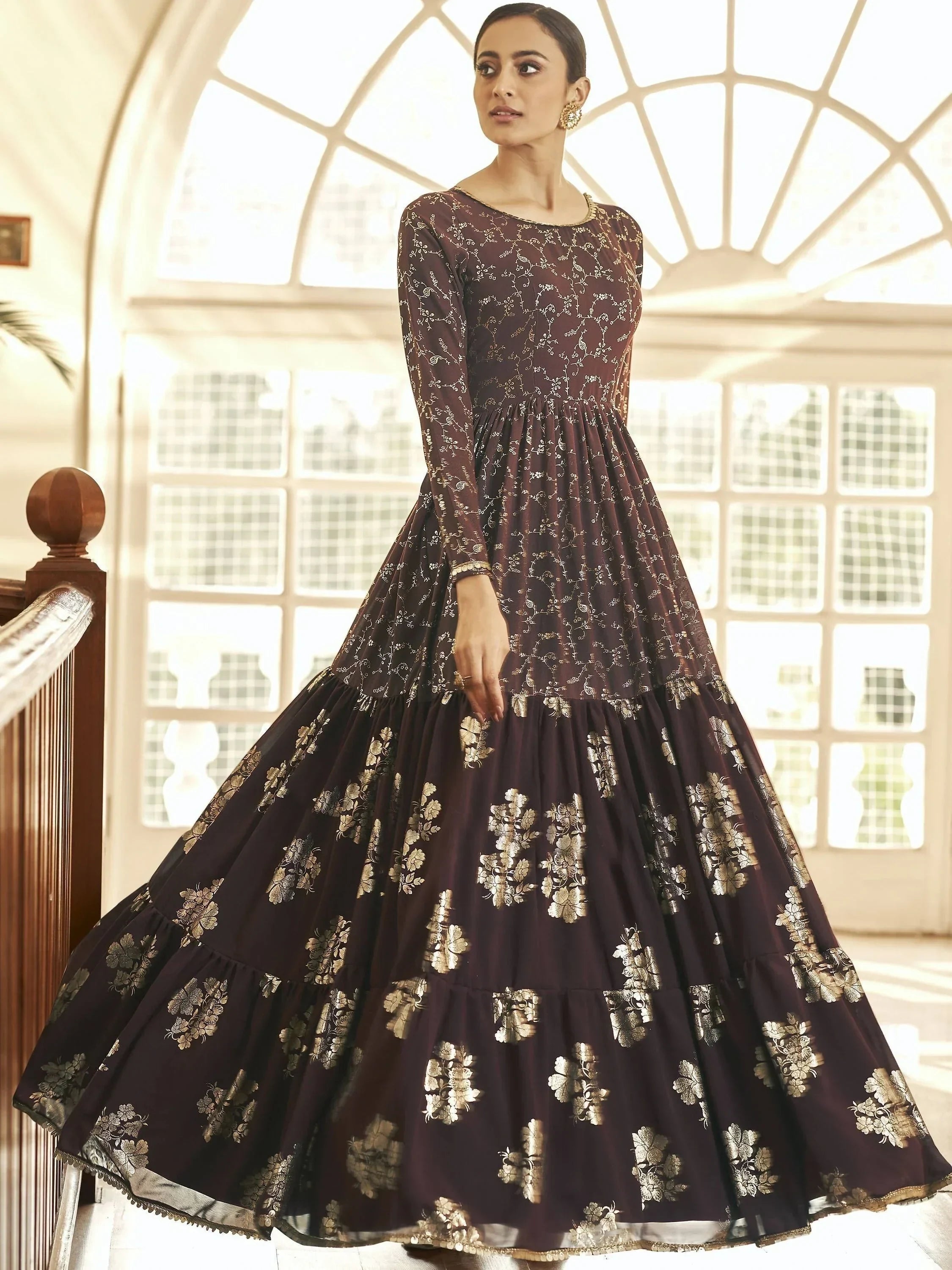 Woman in maroon floral printed ethnic gown with gold motifs, full sleeves, indoor setting