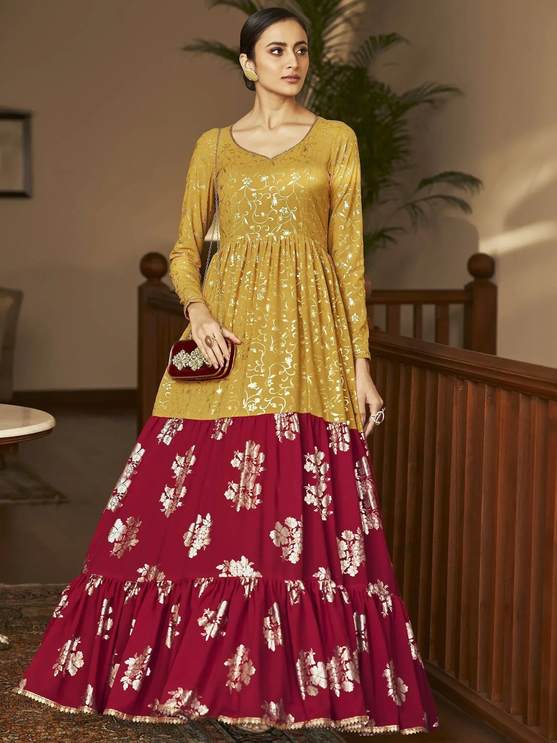 Woman wearing a mustard and maroon ethnic gown with gold floral prints, long sleeves, holding a clutch