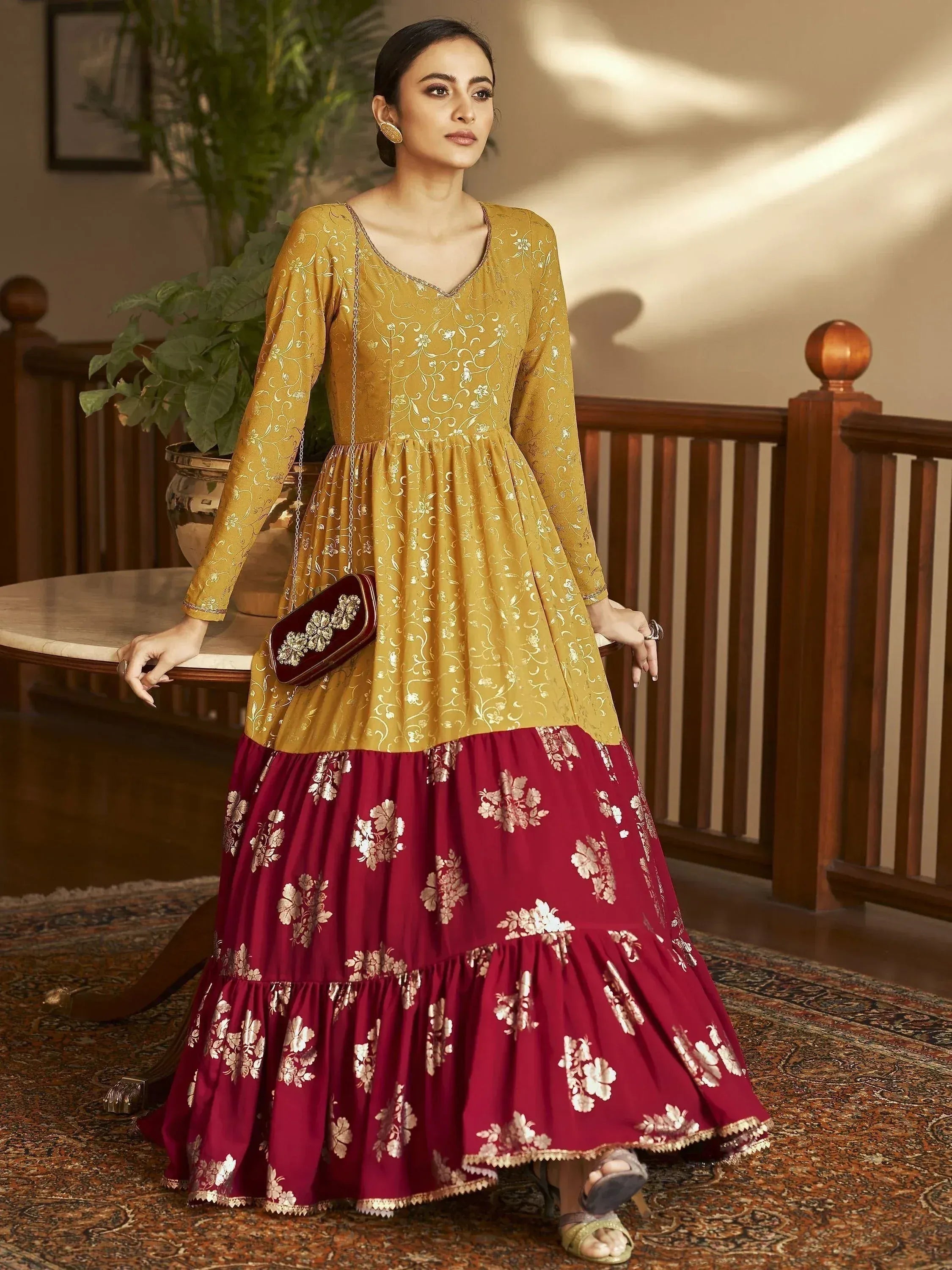 Woman wearing mustard yellow and maroon floral embroidered ethnic gown, standing indoors.