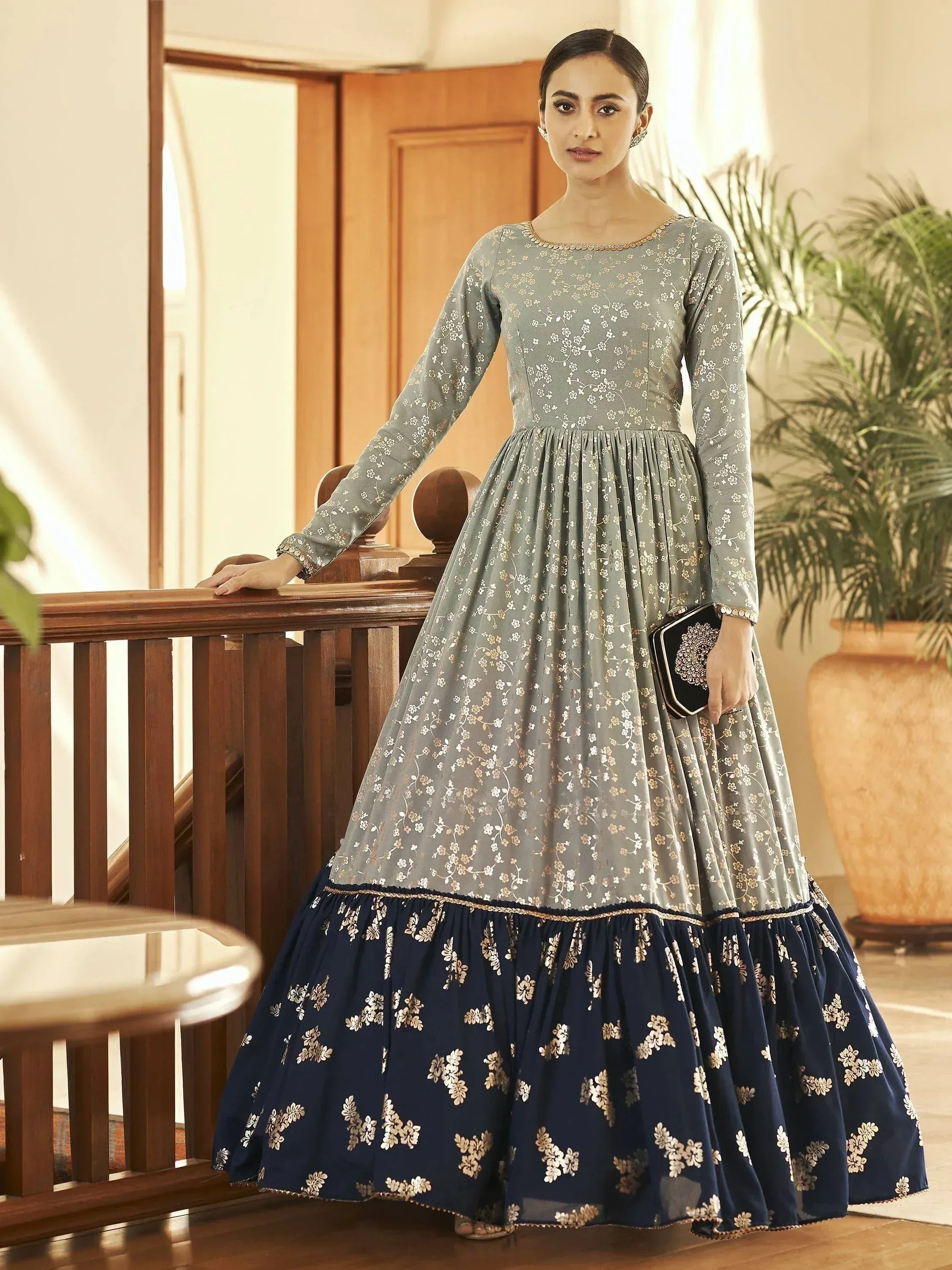 Woman in a long-sleeve floral printed ethnic gown with navy blue and gold detailing indoors