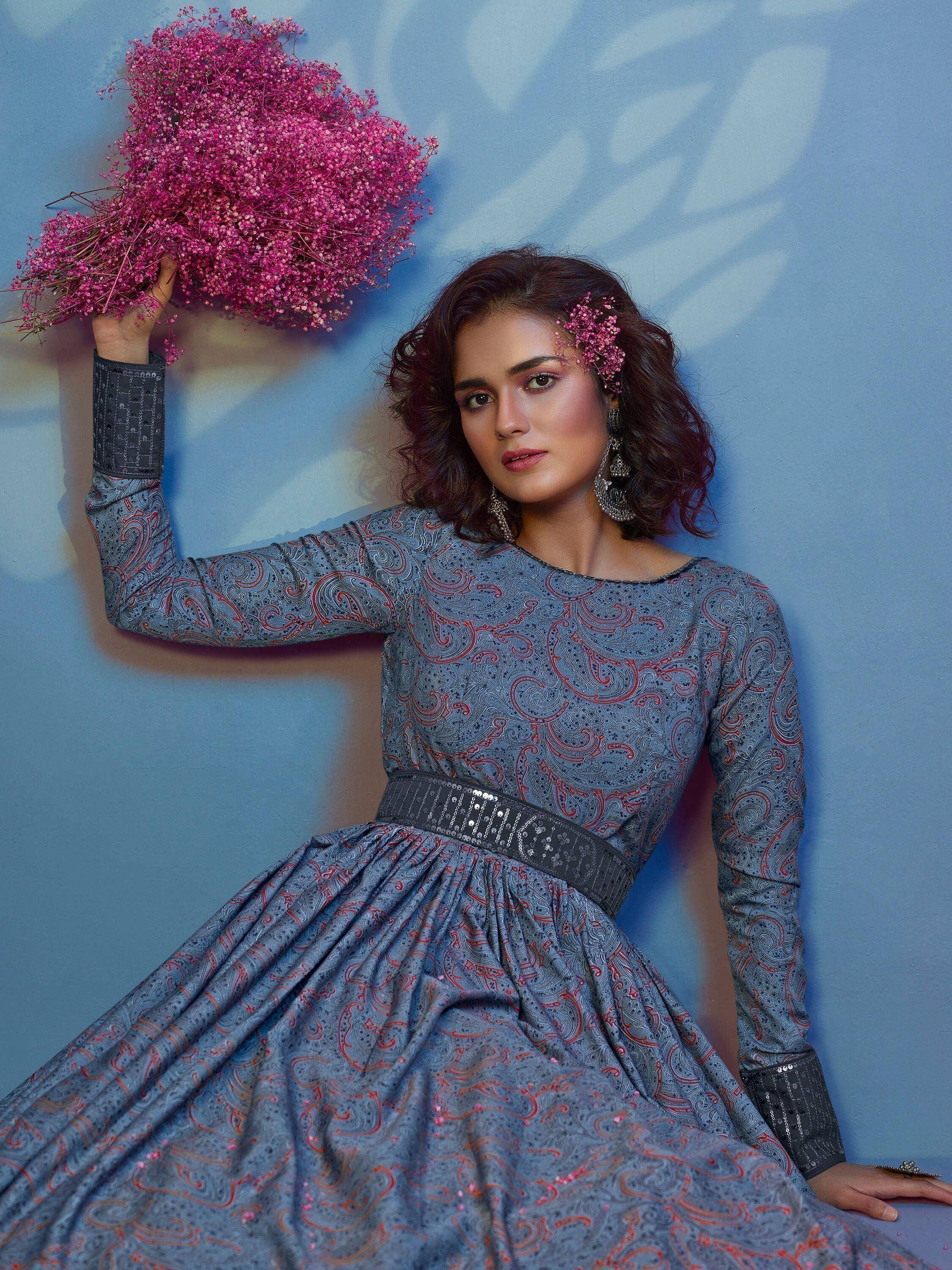 Woman in blue paisley ethnic gown with sequin belt, holding pink flowers, perfect for Indian occasions.