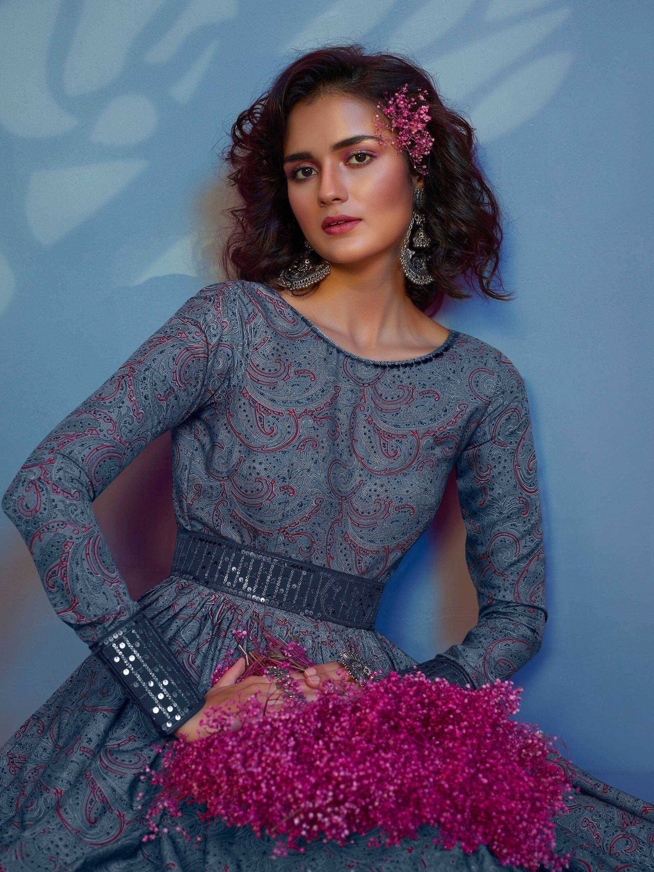 Woman in grey paisley ethnic gown with sequin belt, holding pink flowers, styled with jhumka earrings