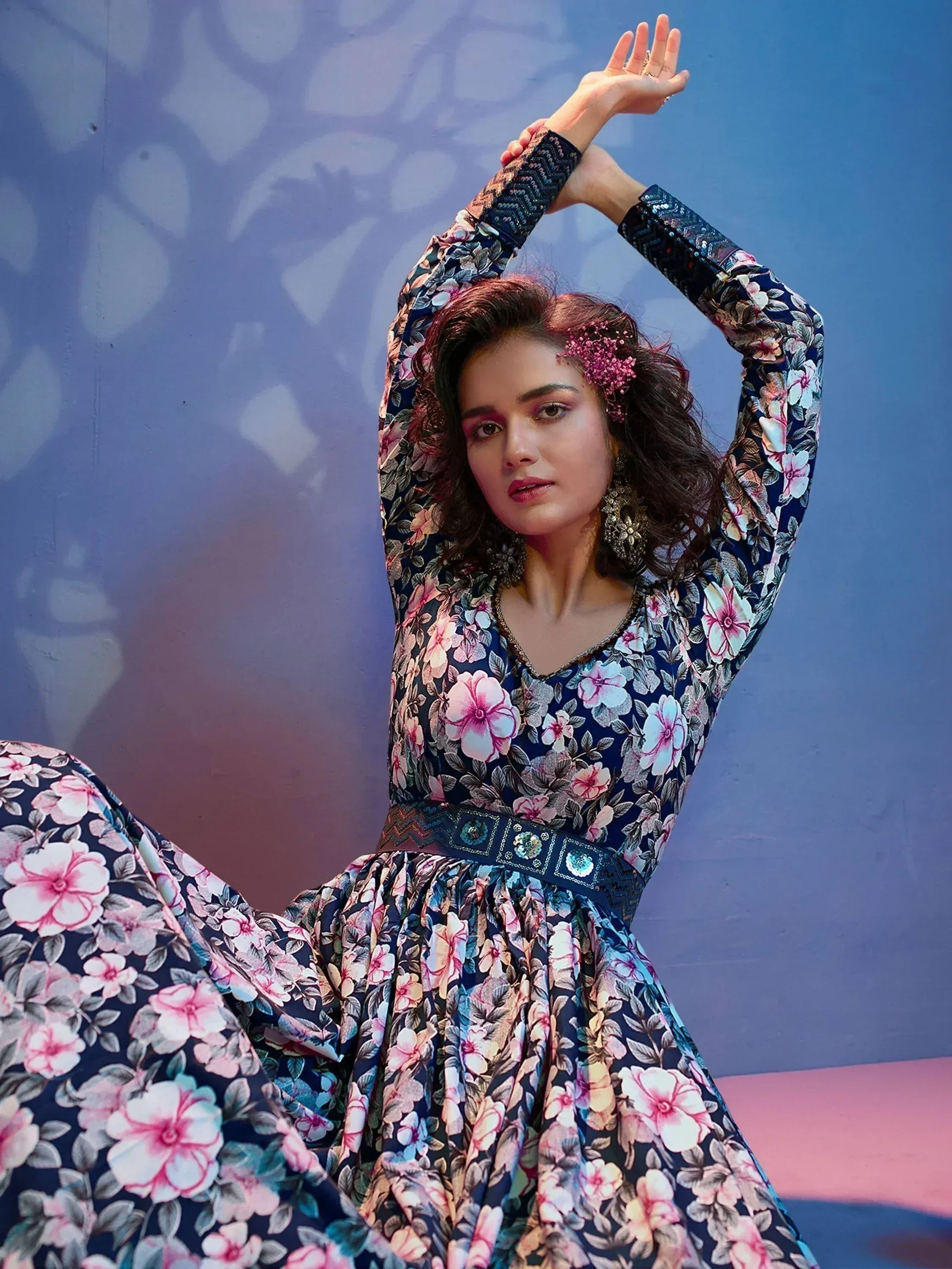 Woman in a navy blue floral ethnic gown with long sleeves and decorative belt, seated indoors