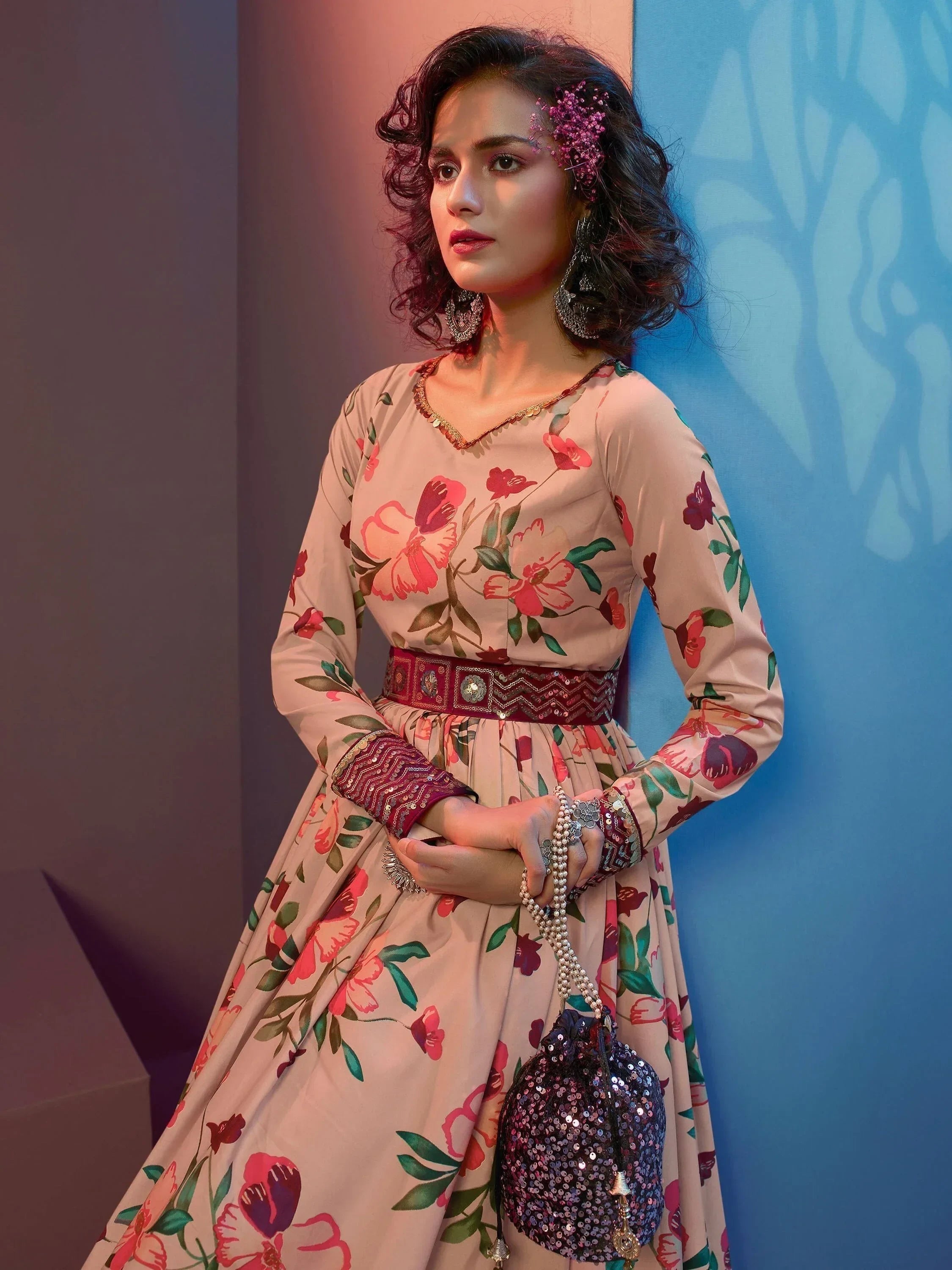 Woman in floral long-sleeve ethnic gown with printed belt, holding sequin potli bag