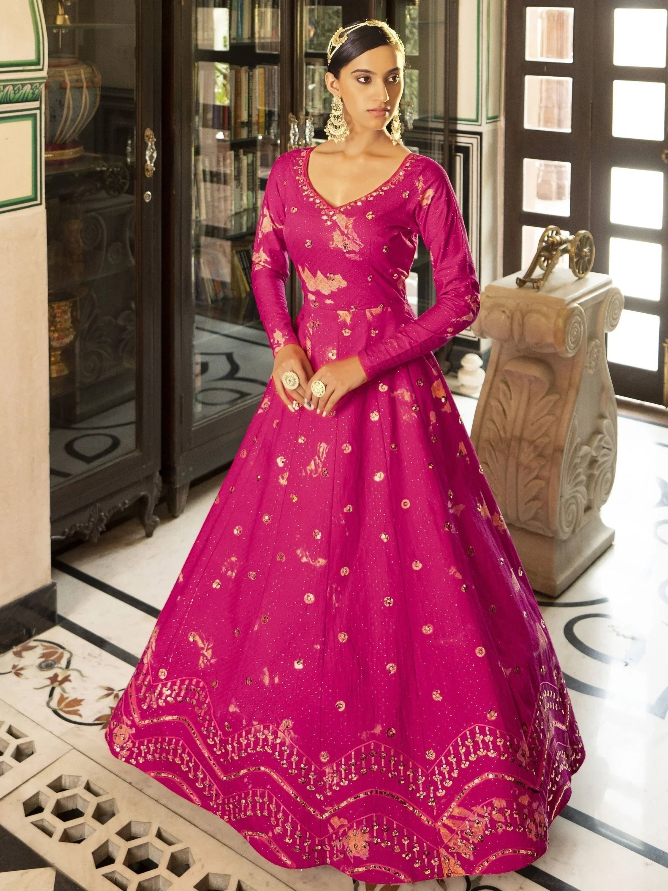 Woman in a pink embroidered ethnic gown with gold accents, standing indoors