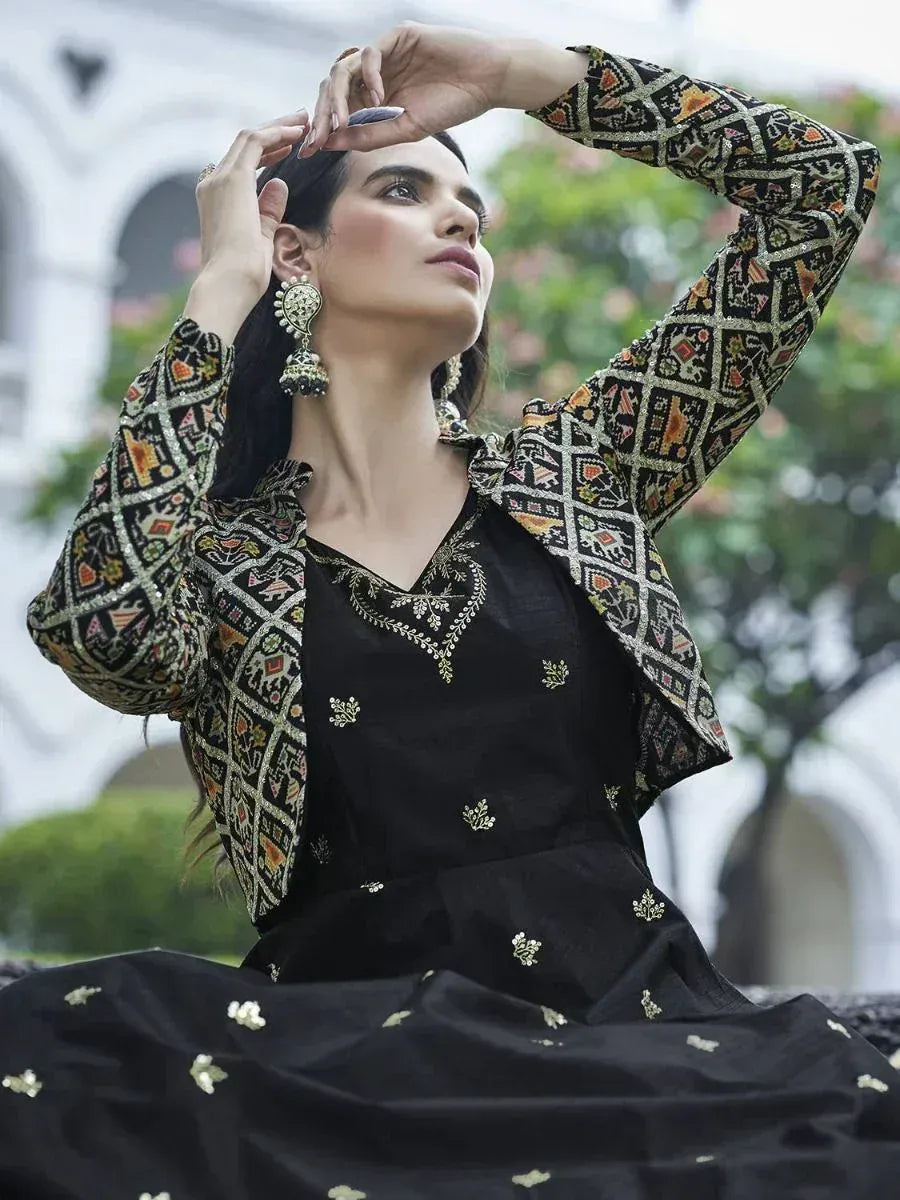 Woman in a black embroidered ethnic gown with patterned long jacket, outdoor setting