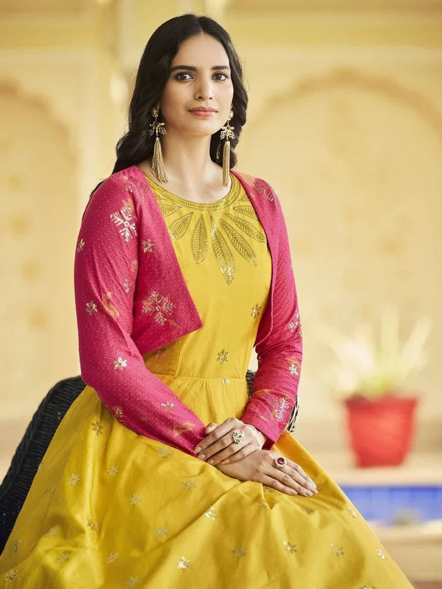 Woman in yellow ethnic gown with pink embroidered jacket and gold jewelry, traditional Indian attire