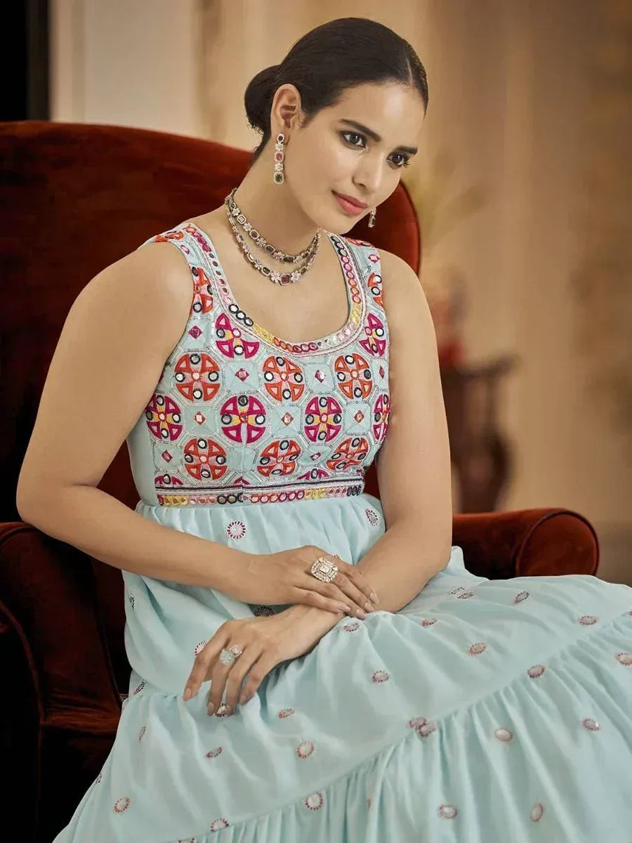 Woman in light blue embroidered ethnic gown with colorful mirror work, styled with jewelry for festive occasions