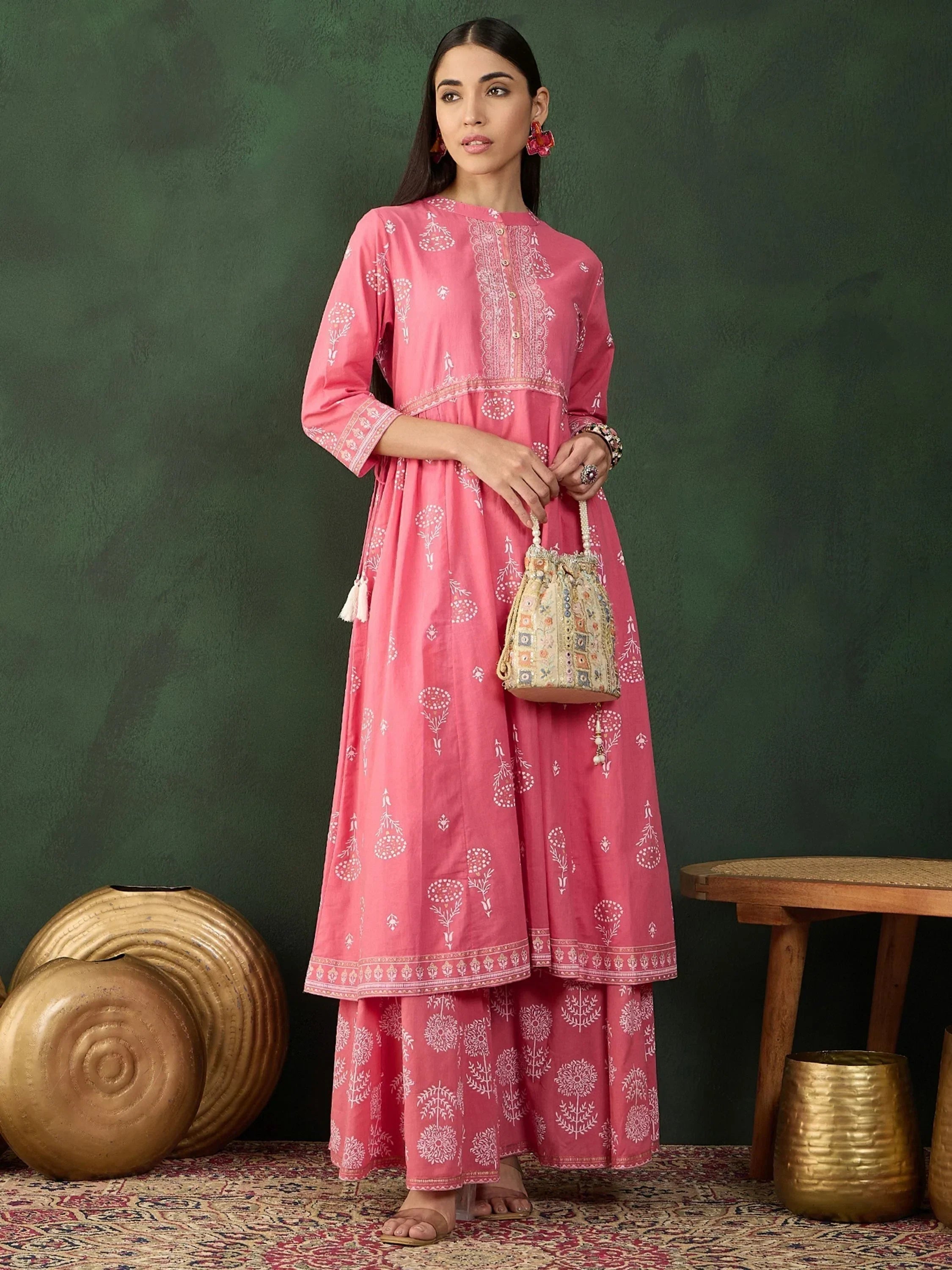 Woman wearing pink printed Anarkali kurta set, holding embroidered potli bag, traditional ethnic wear