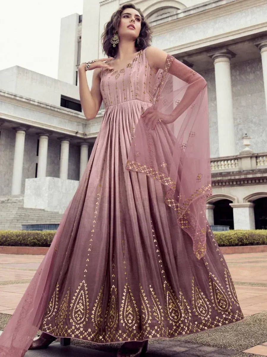 Woman wearing mauve embroidered ethnic gown with dupatta, standing outdoors.