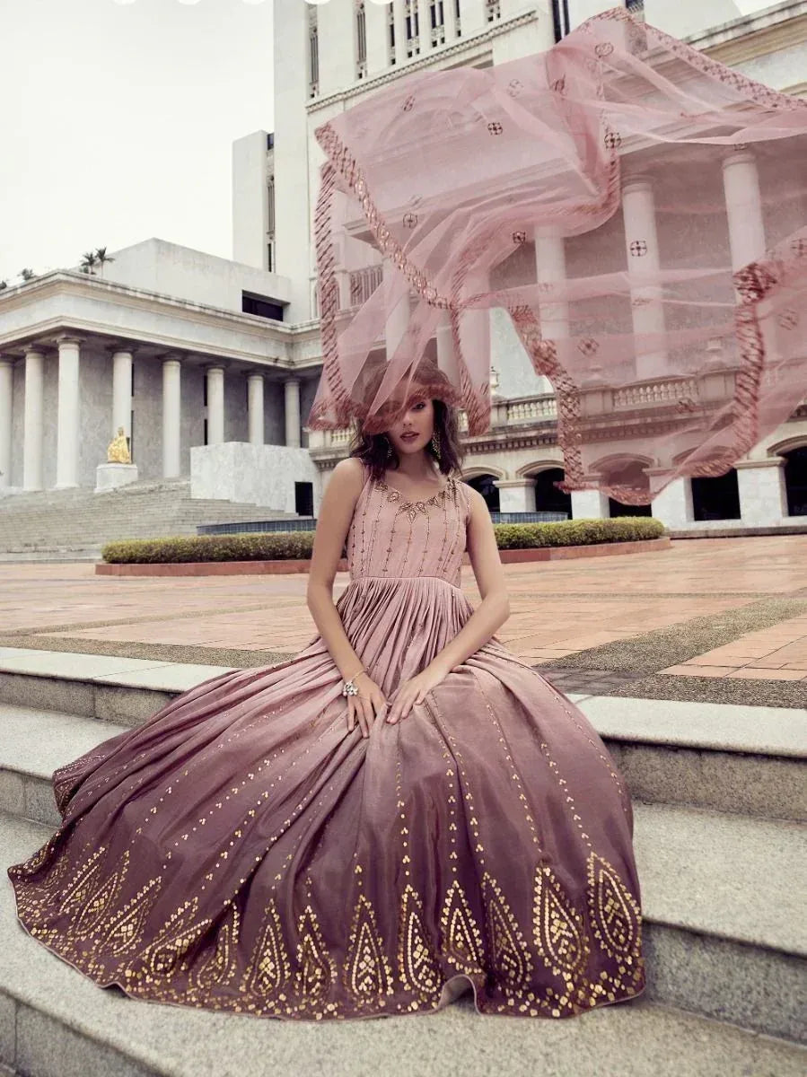 Woman in a pink and gold embroidered ethnic gown with matching dupatta, sitting outdoors